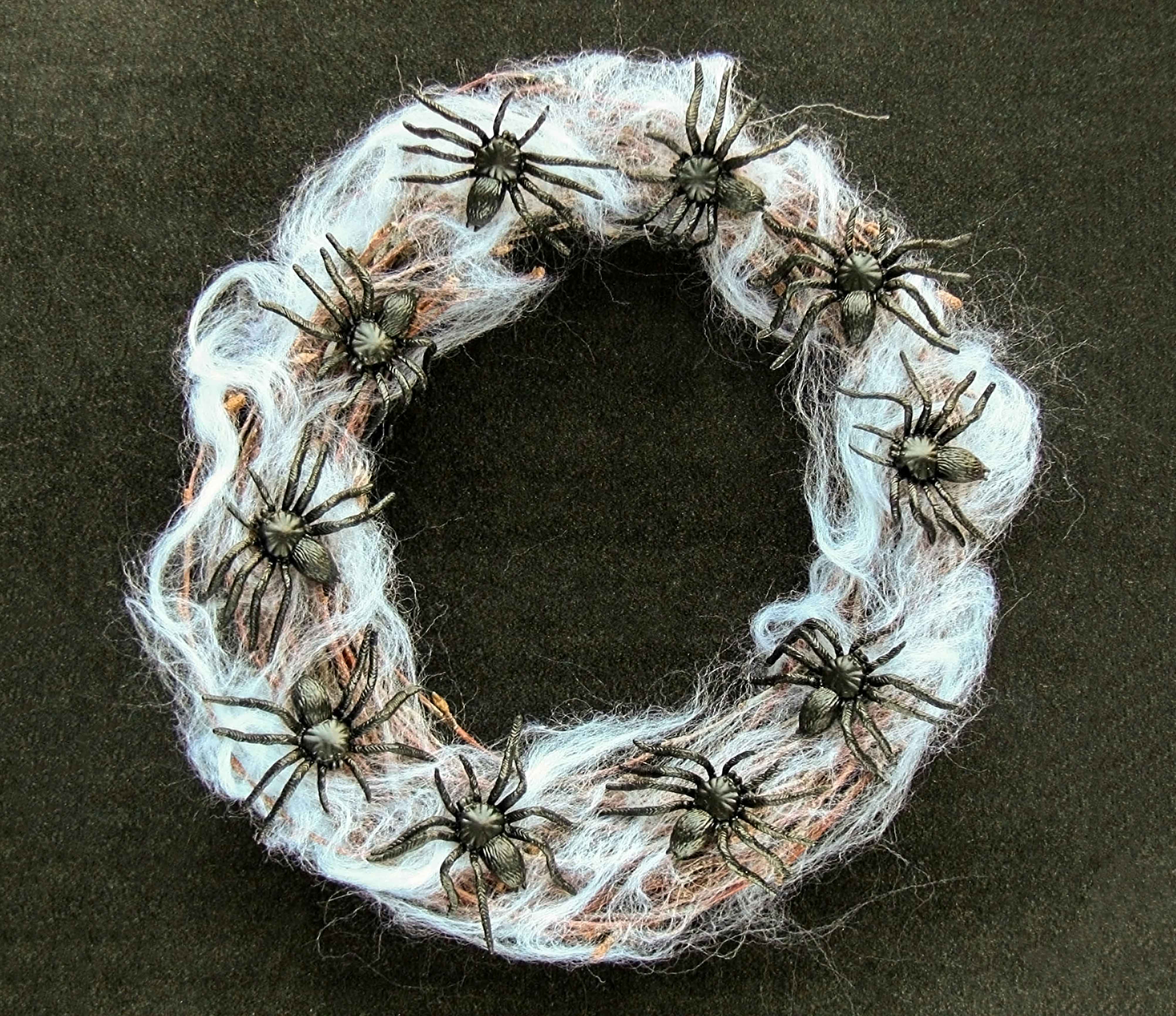 A wreath if spider webs and plastic spiders on a wood surface.