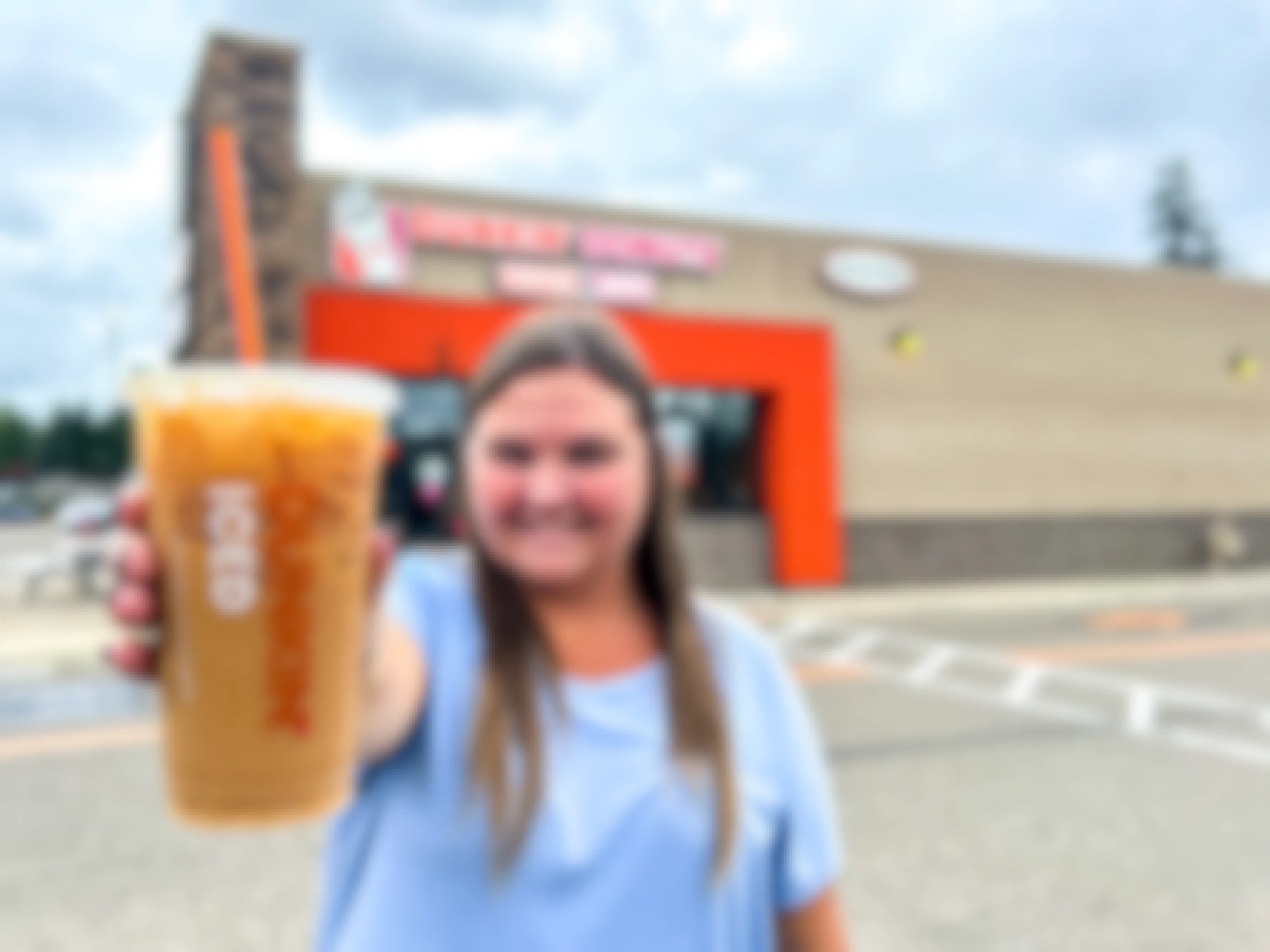 a person standing outside of dunkin with an iced coffee