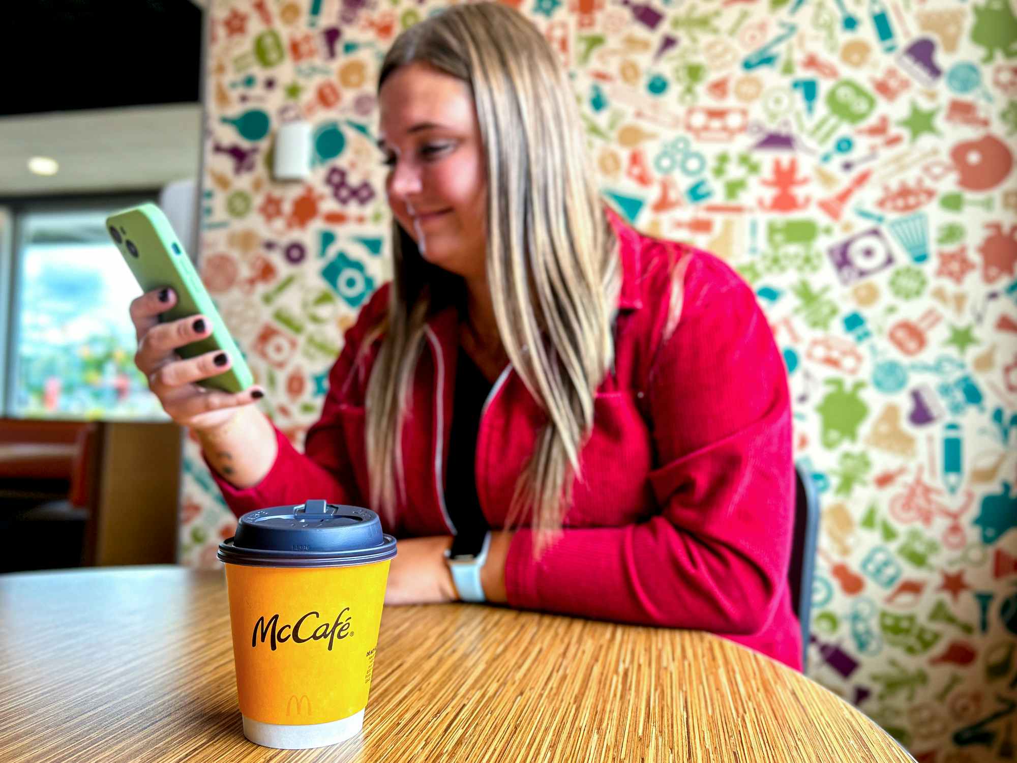 a person looking at their phone inside of mcdonalds sitting next to a cup of coffee