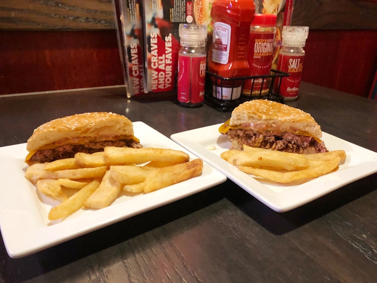 Two plates sitting on a table at Red Robin, each with half of a burger and some fries. On the table in the background are seasonings, ketchup, and some menus tucked away.
