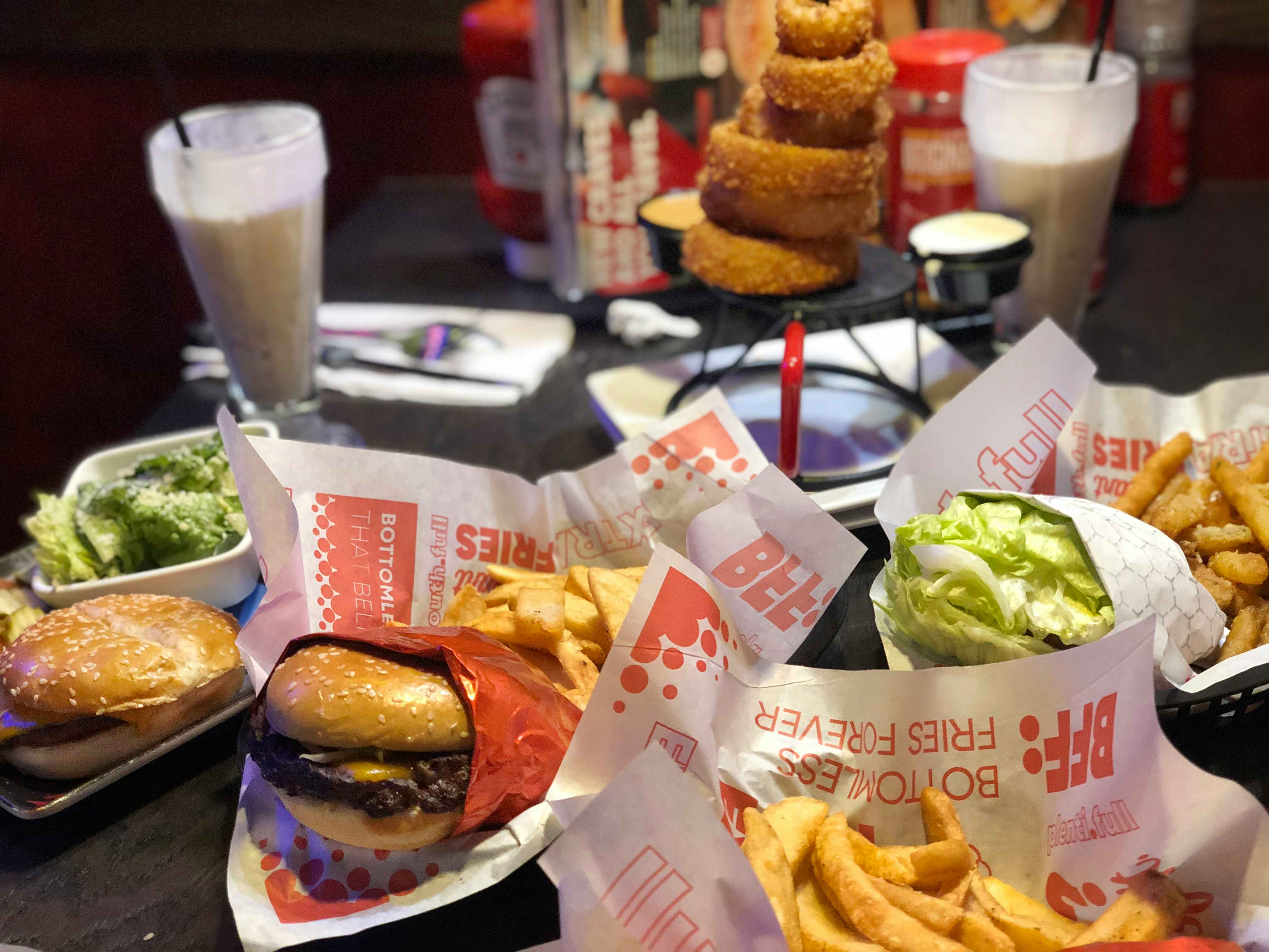 A table at Red Robin with multiple plates of food, including burgers, fries, broccoli, a tower of onion rings, and two milkshakes.