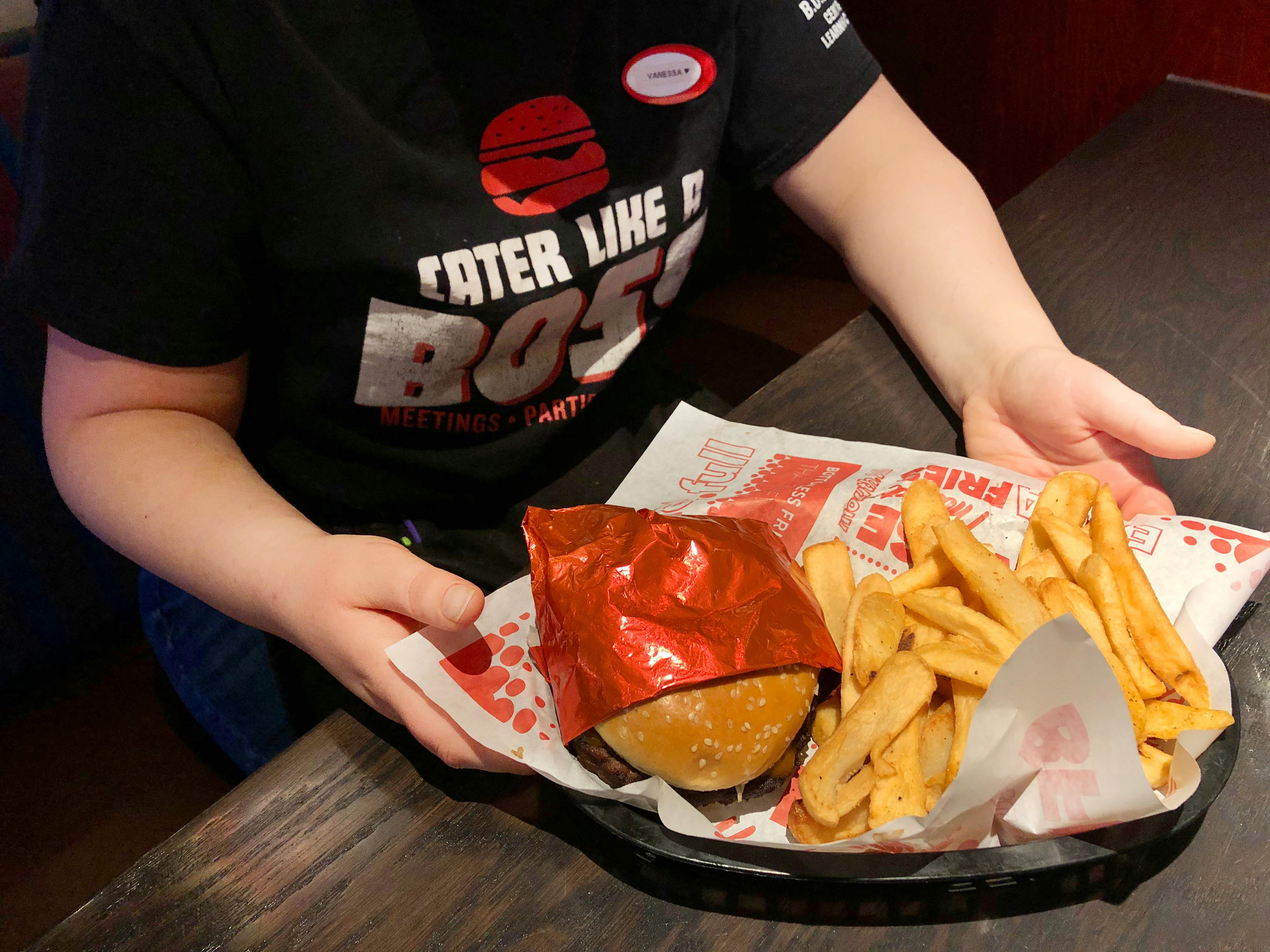 A Red Robin employee sitting in a booth at Red Robin, holding a basket with a burger and fries.