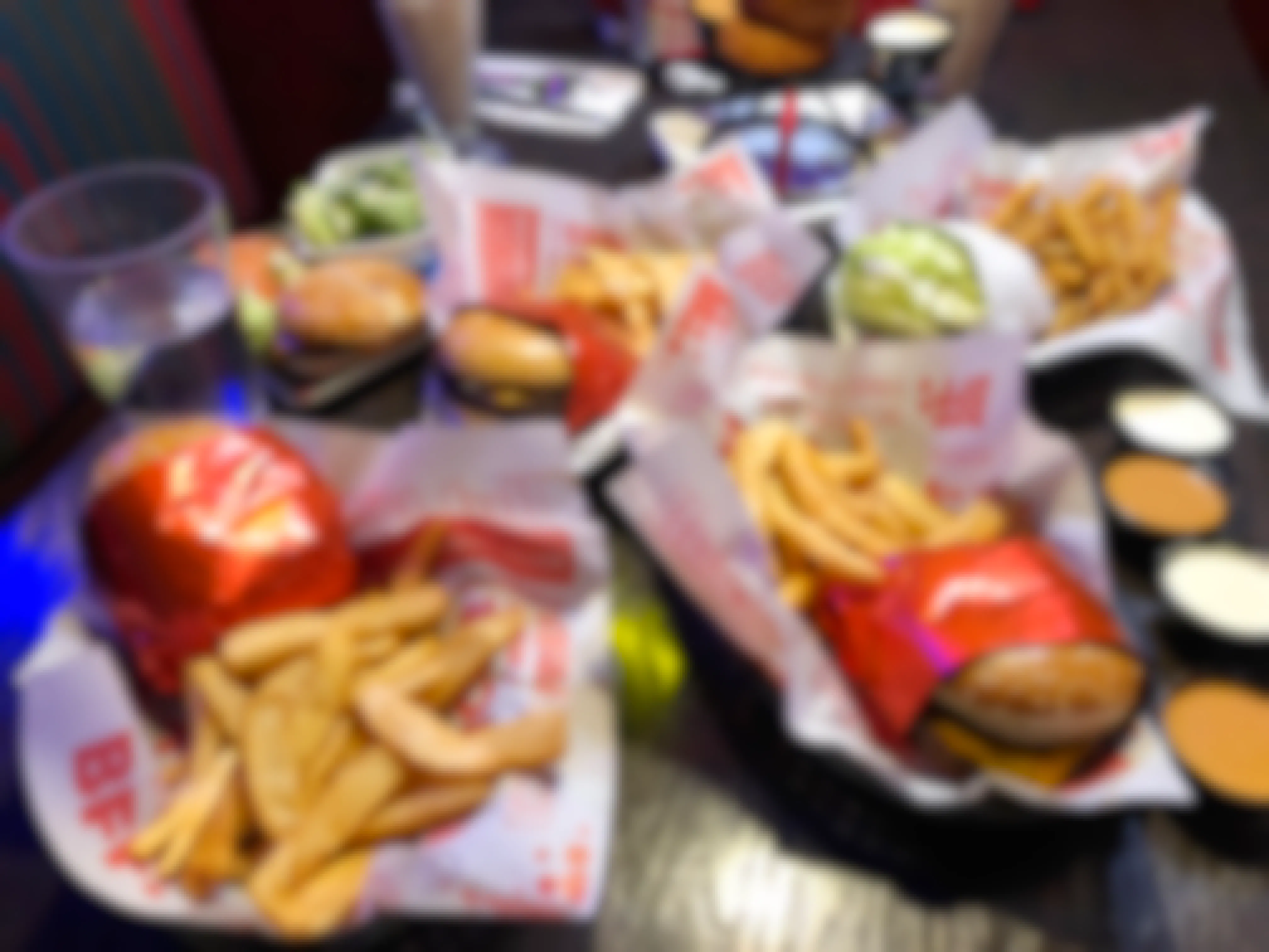 A table at Red Robin with multiple plates of food, including burgers, fries, broccoli, a tower of onion rings, a milkshake, and several dipping cups.