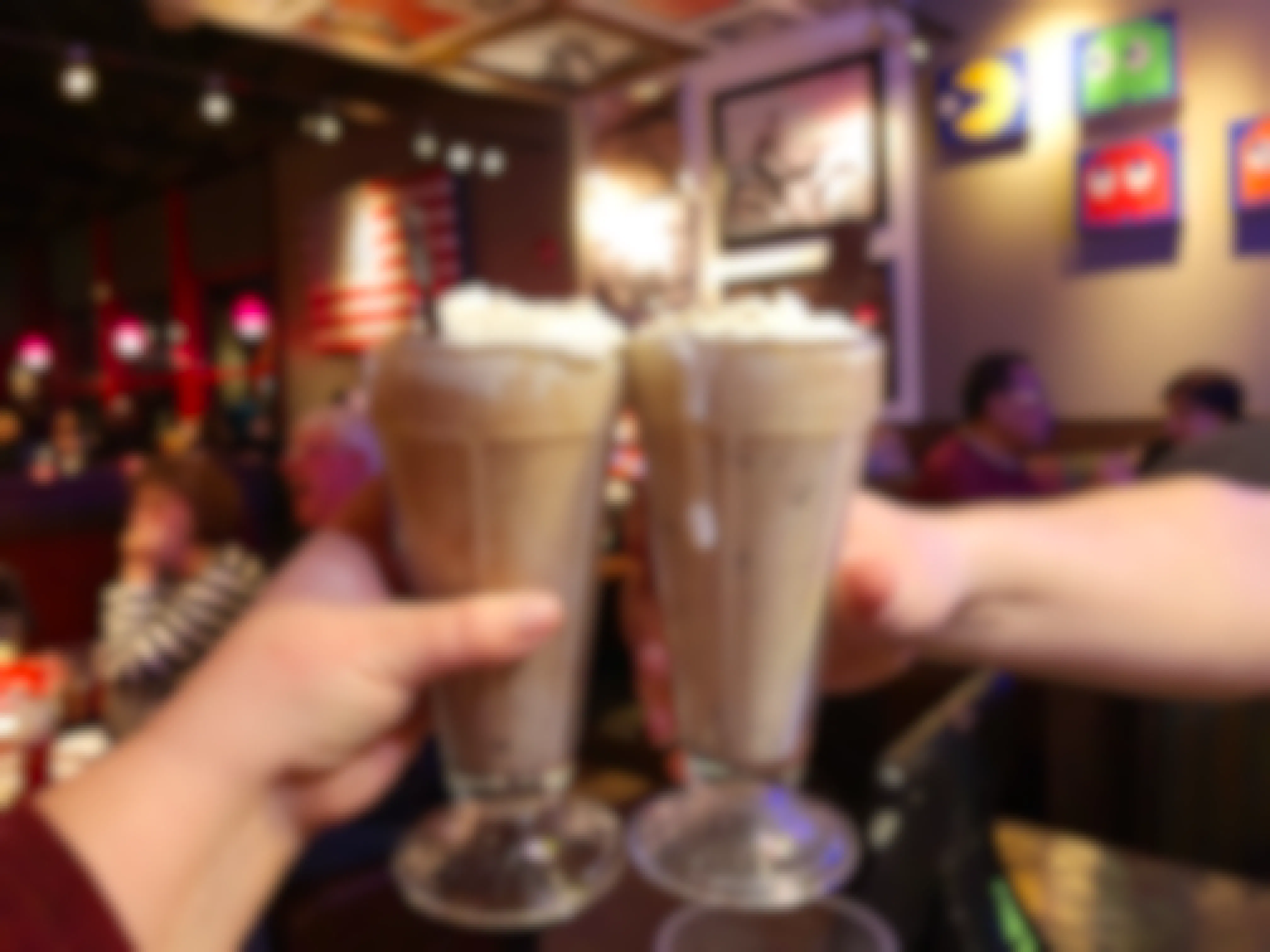 Two people's hands lifting up their milkshakes to cheers inside a Red Robin.