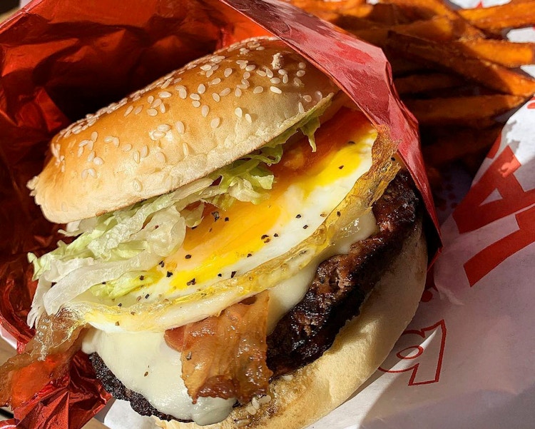 A close-up of a Red Robin burger with bacon and an egg on it, sitting in a basket with fries.