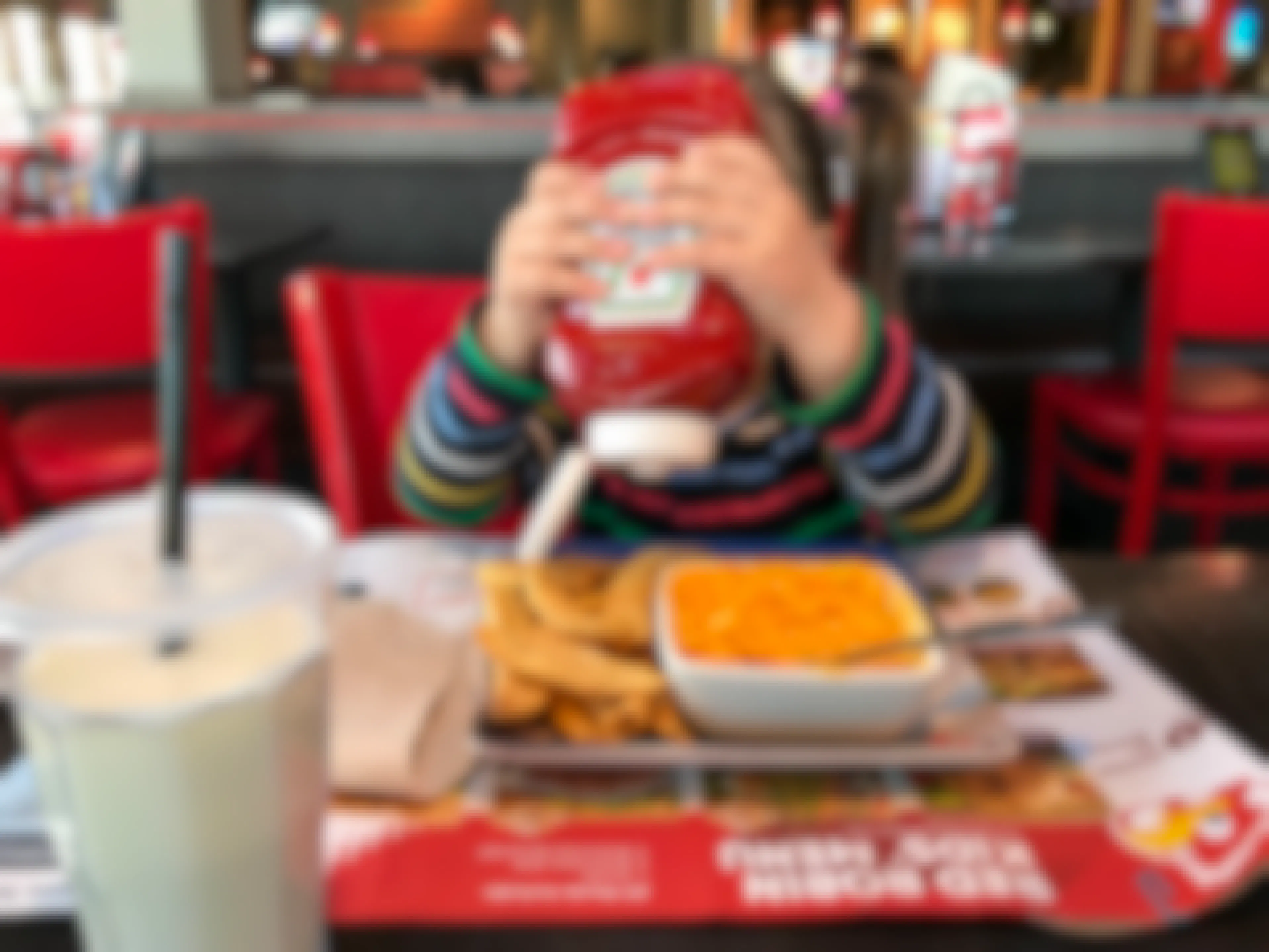 A child squeezing a bottle of Heinz ketchup onto a plate of fries and mac and cheese in front of her at a booth at Red Robin.