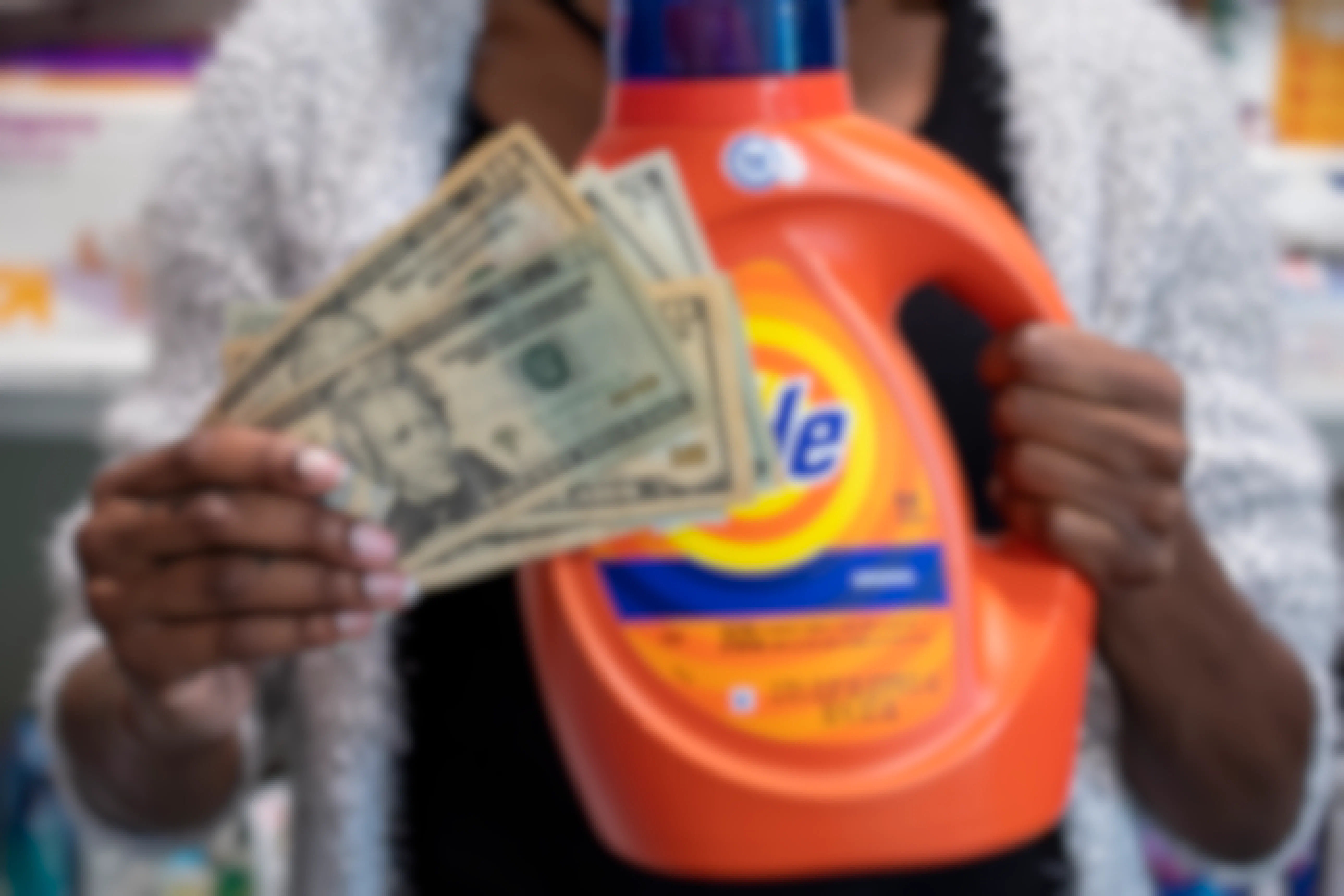 A person holding a stack of cash next to a bottle of Tide laundry detergent.