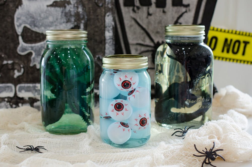 Large mason jars filled with water, food coloring, and dish soap, containing dollar tree plastic eyeballs, spider, and snake.
