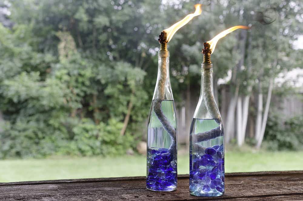 Two lit tiki torches made of wine bottles.