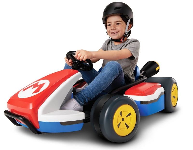 A kid riding on a Mario Kart 24V Ride-On Racer on a white background.