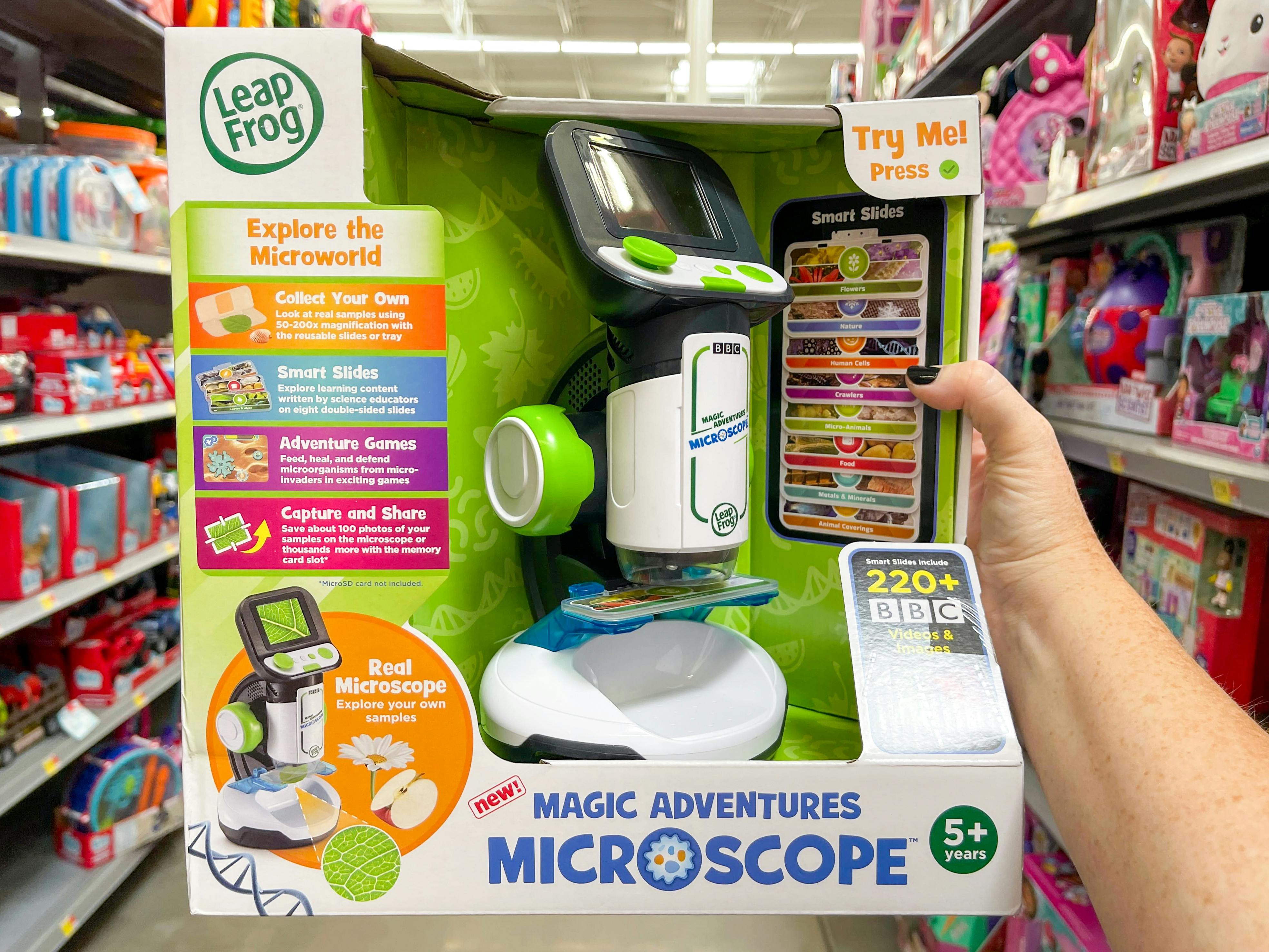 A person's hand holding a Leapfrog Magic Adventures Microscope in a toy aisle
