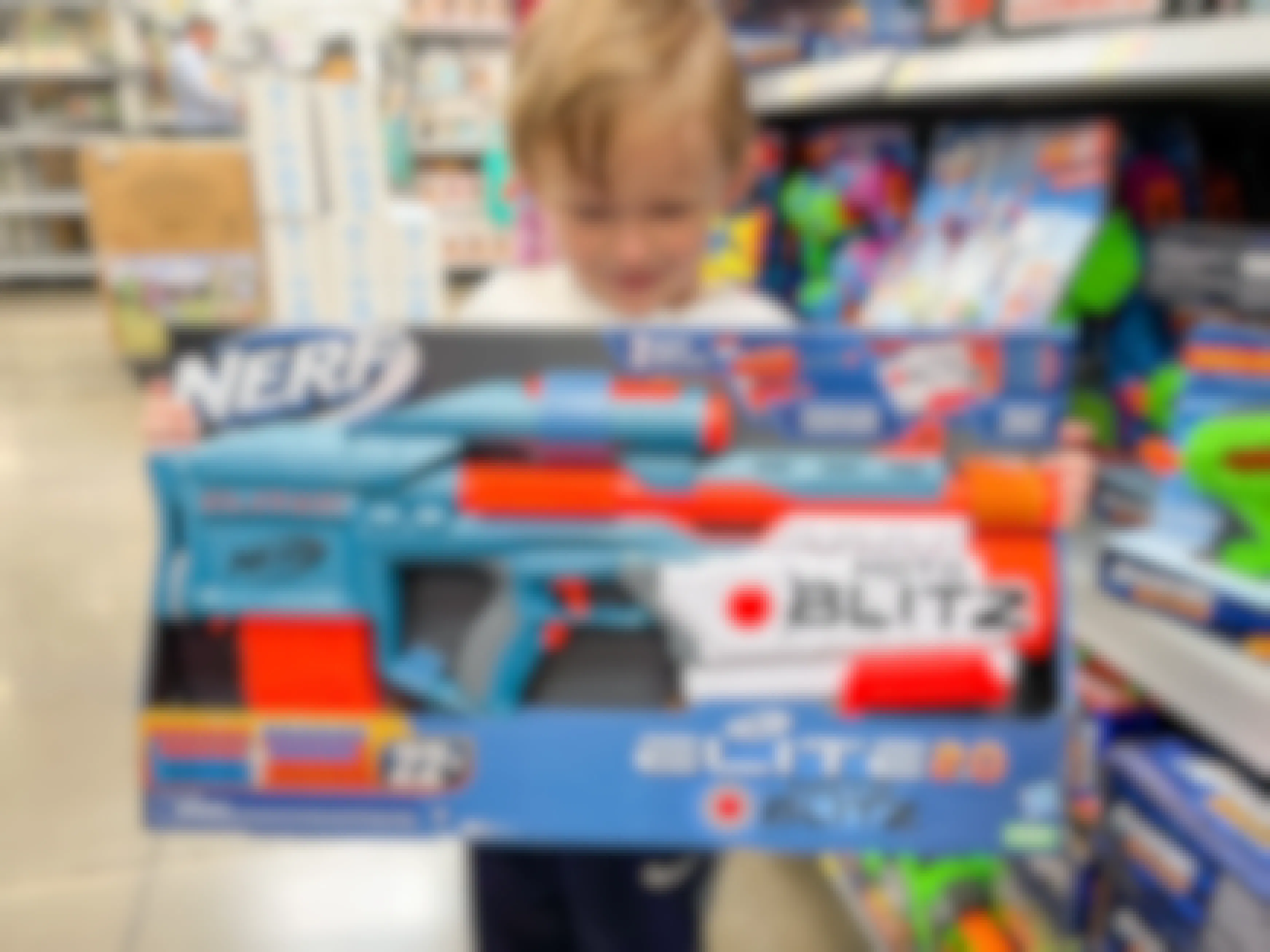 A little boy holding a Nerf Elite Motoblitz motorized dart blaster in a toy aisle.