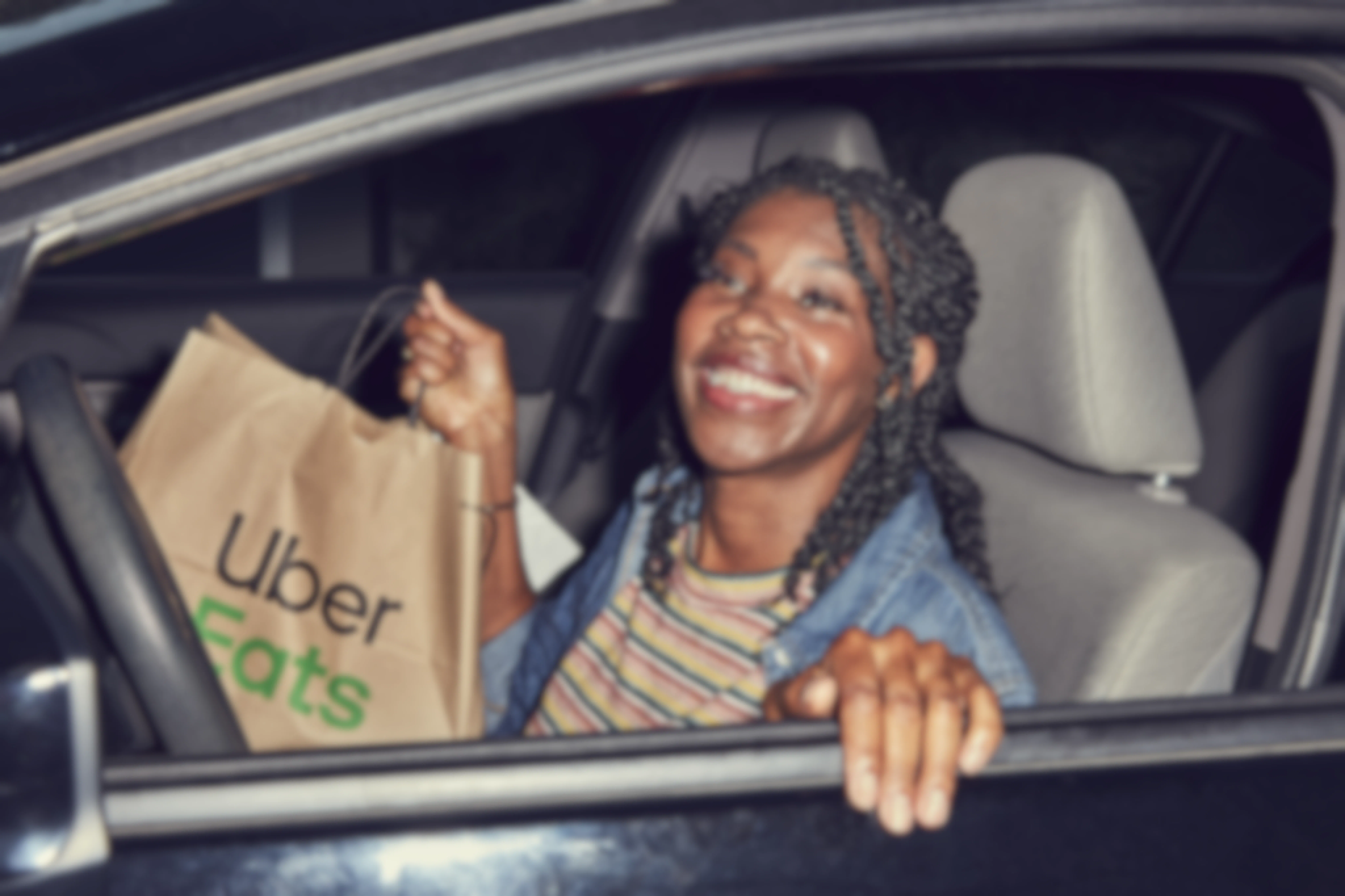 A woman opening the door to her car to exit, holding an Uber eats bag in her hand.