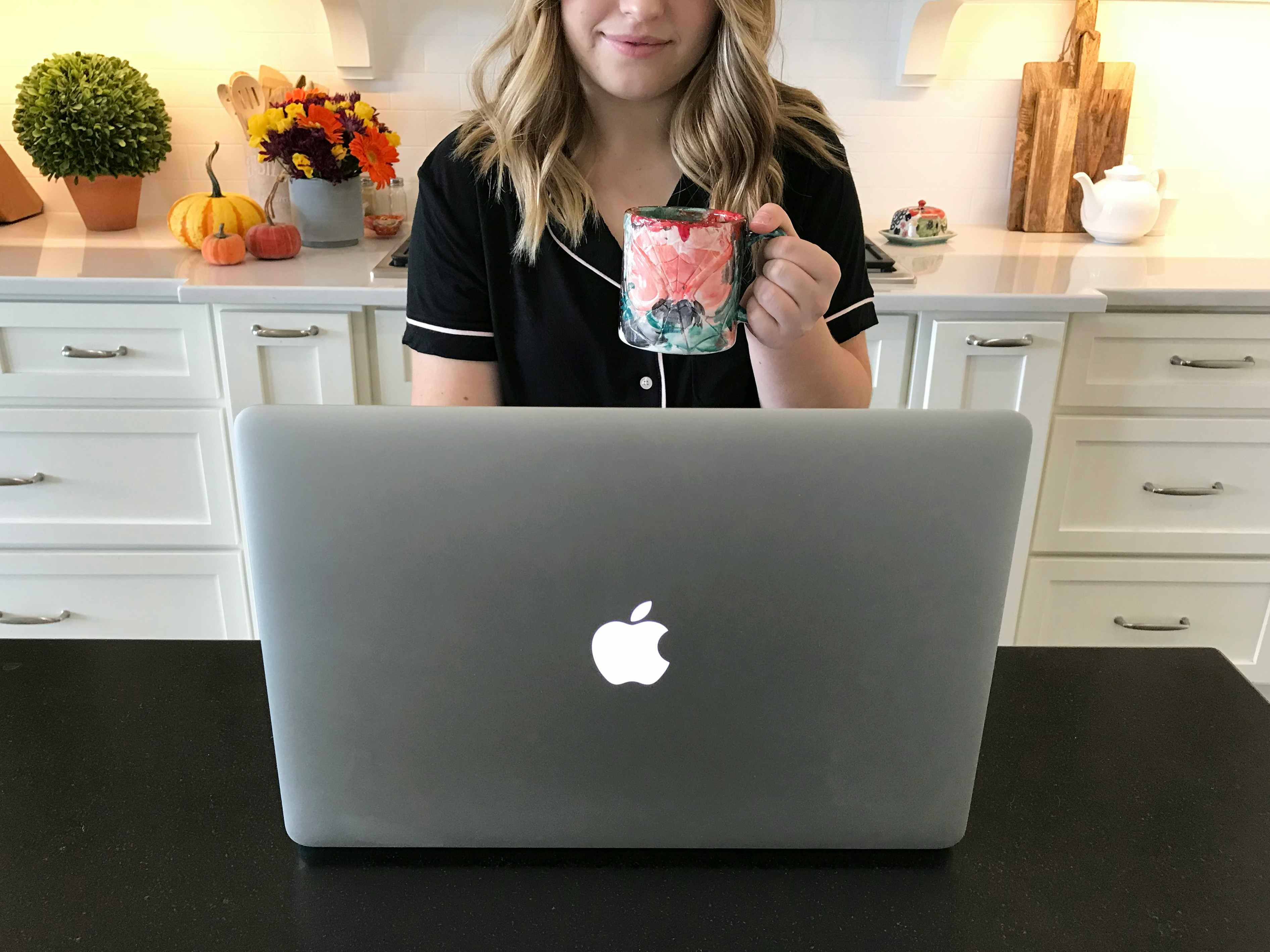 A woman sitting in front of her laptop in her pajamas holding a cup of coffee 