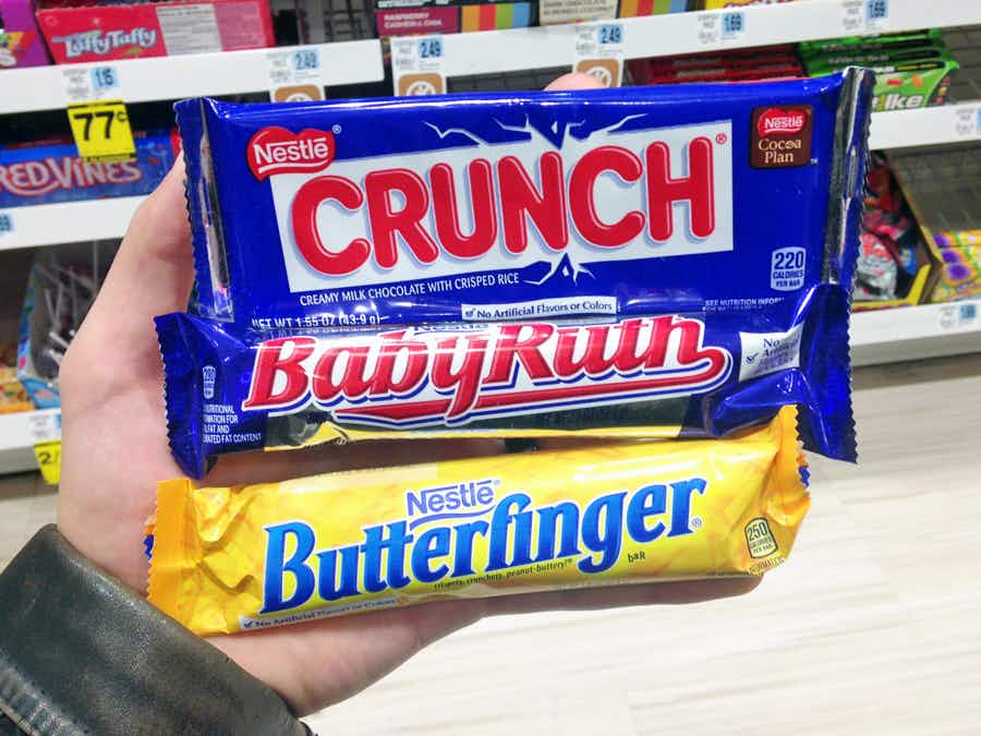 A person's hand holding some full size candy bars in Rite Aid.