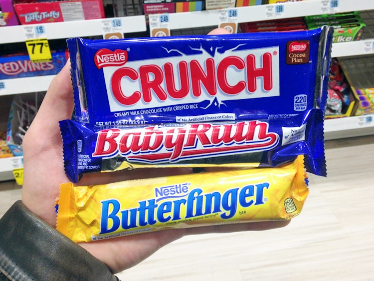 A person's hand holding some full size candy bars in Rite Aid.