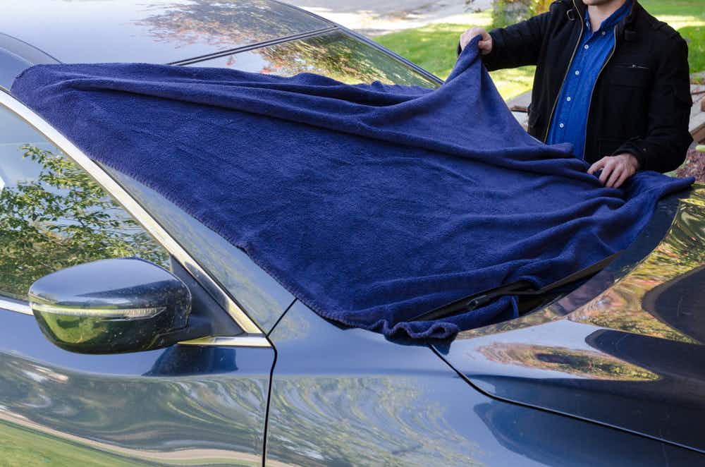 A person putting a blanket over a car window. 