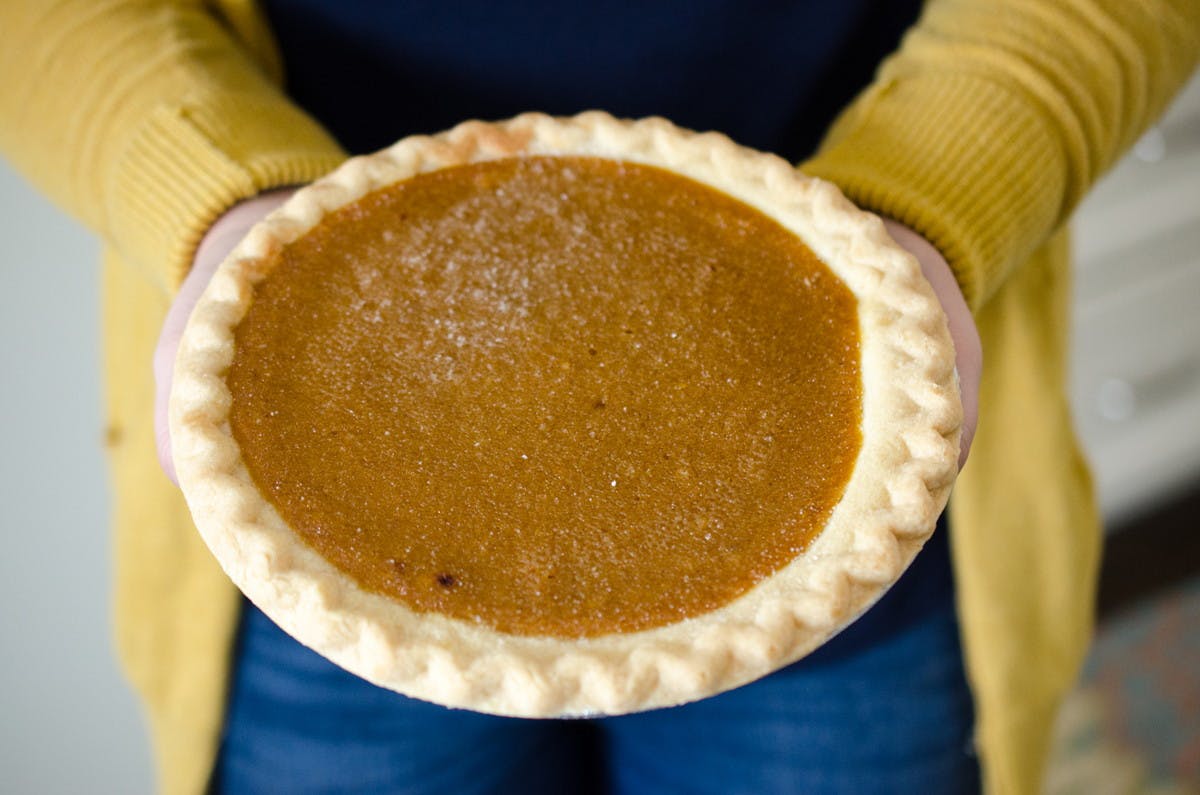 A person holding out a pumpkin pie.