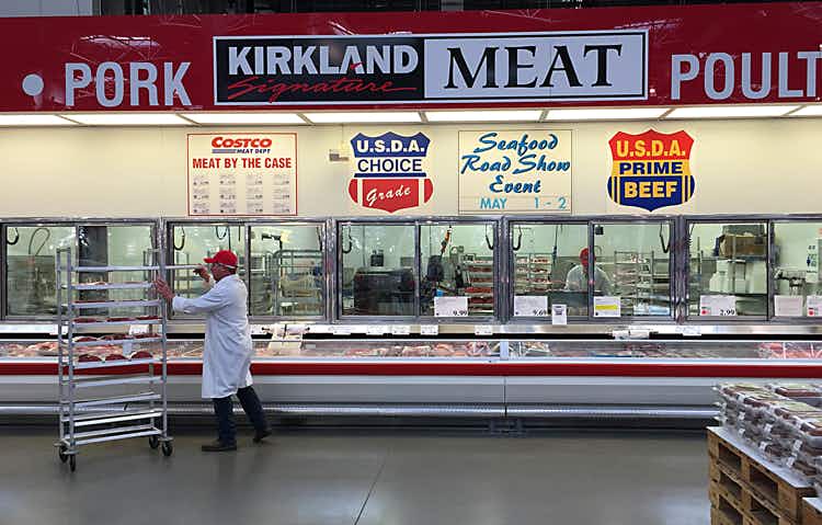 zoomed out shot of costco meat section with a Kirkland meat sign and butcher in white coat
