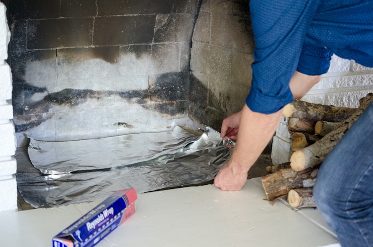 A person putting foil in the bottom of a fireplace.