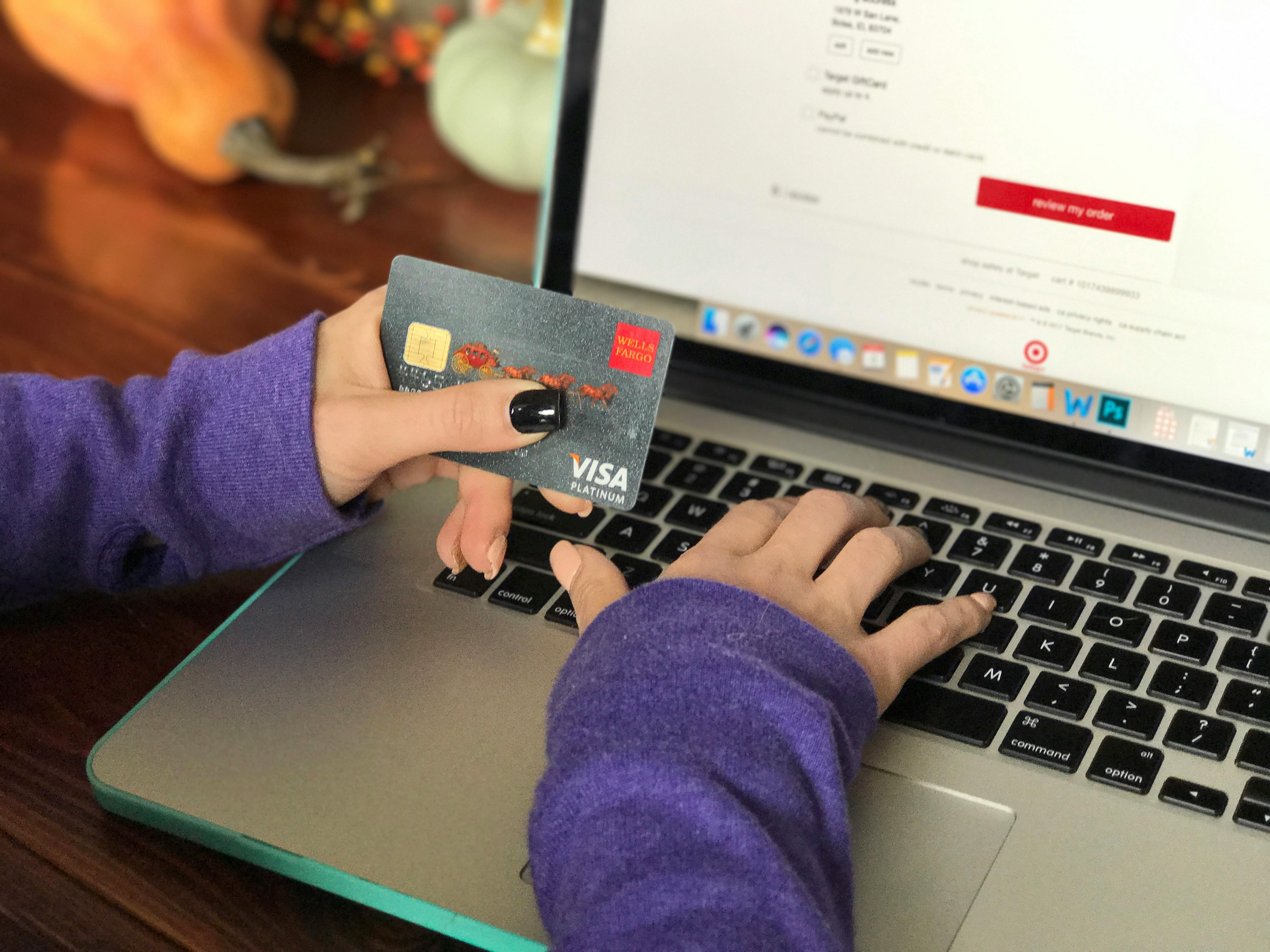 A person using a laptop, holding their credit card.