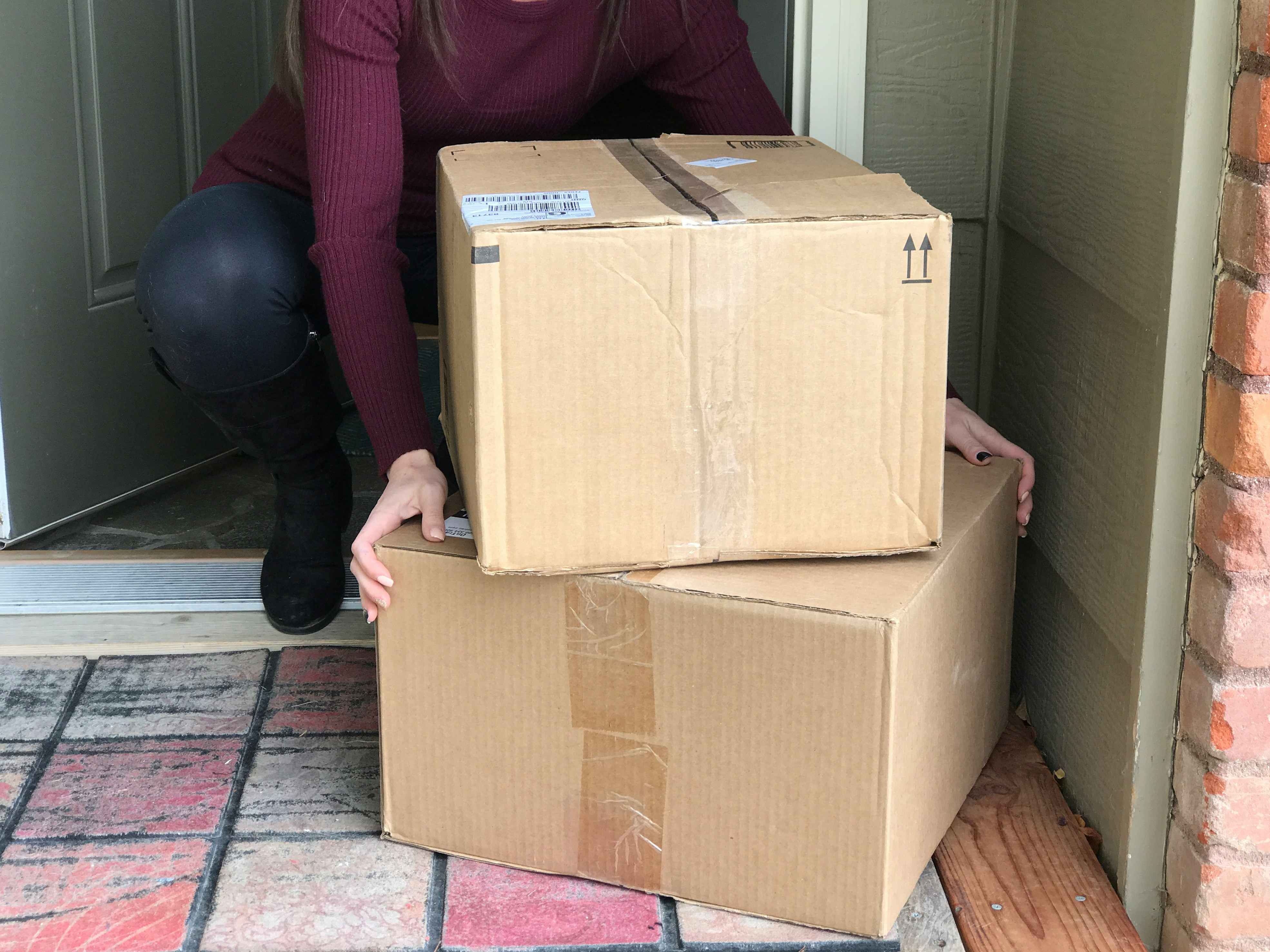 A person bending down to pick up some packages off of the front porch