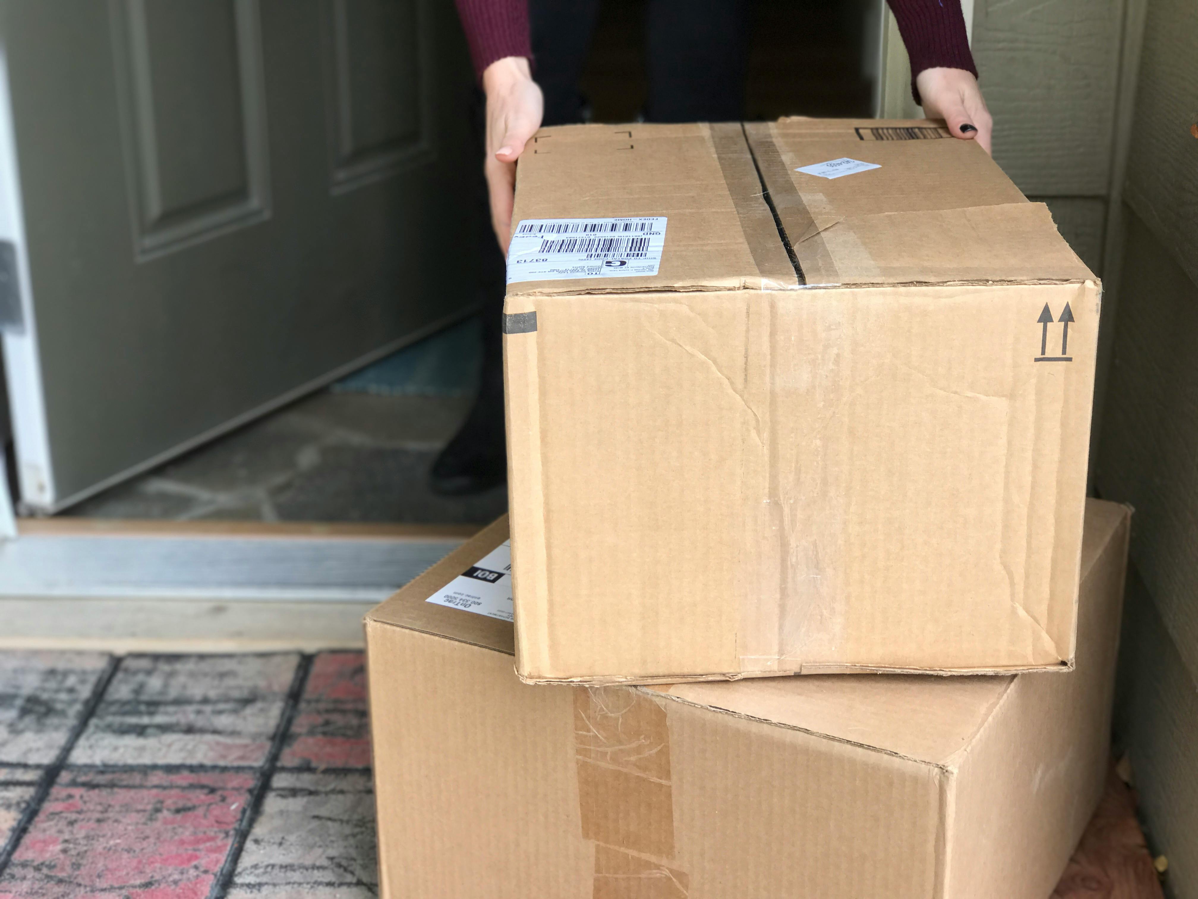 A person picking up a box from two stacked on the front porch.