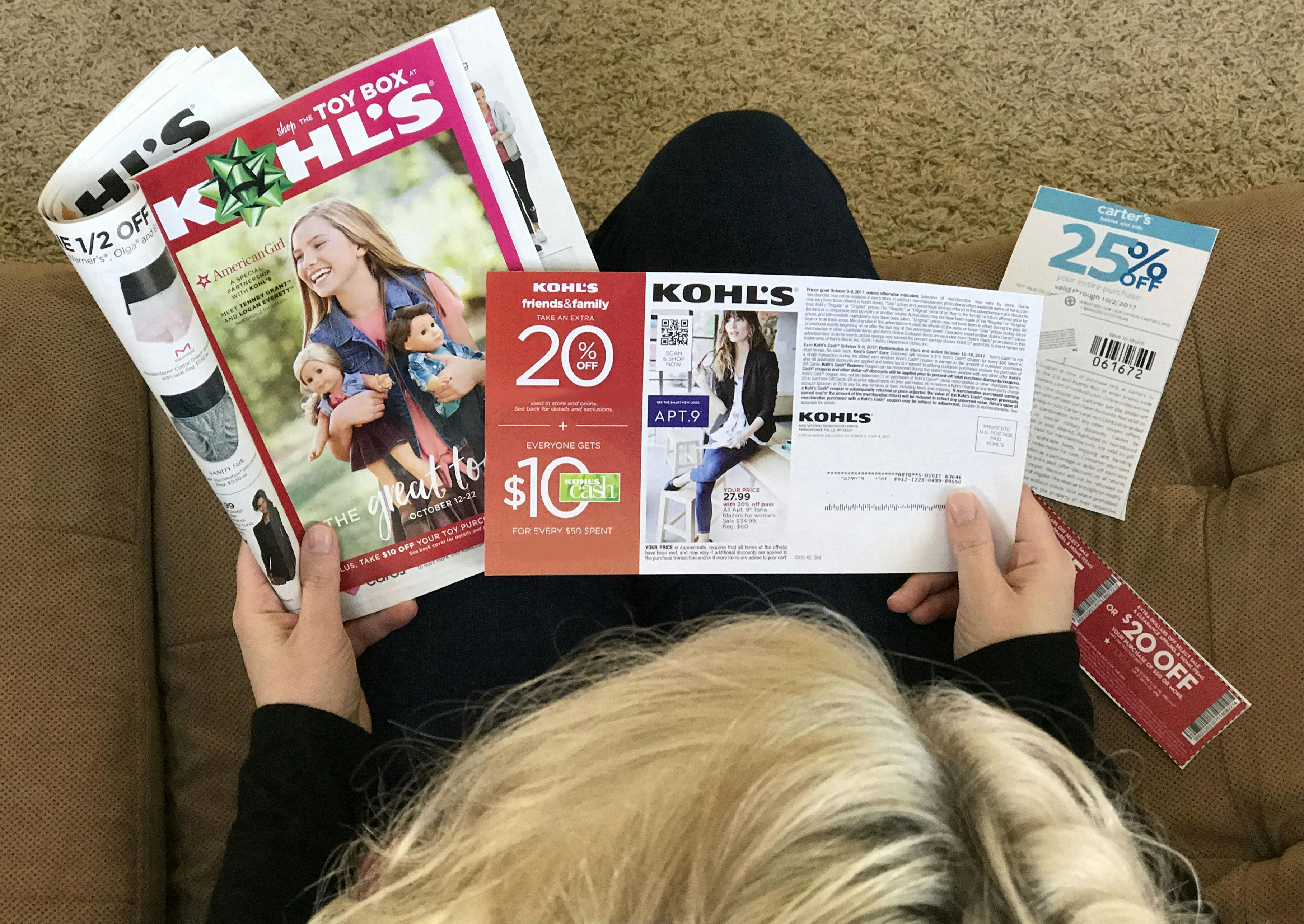 A person sitting on a couch, looking at some Kohl's coupons and an ad.