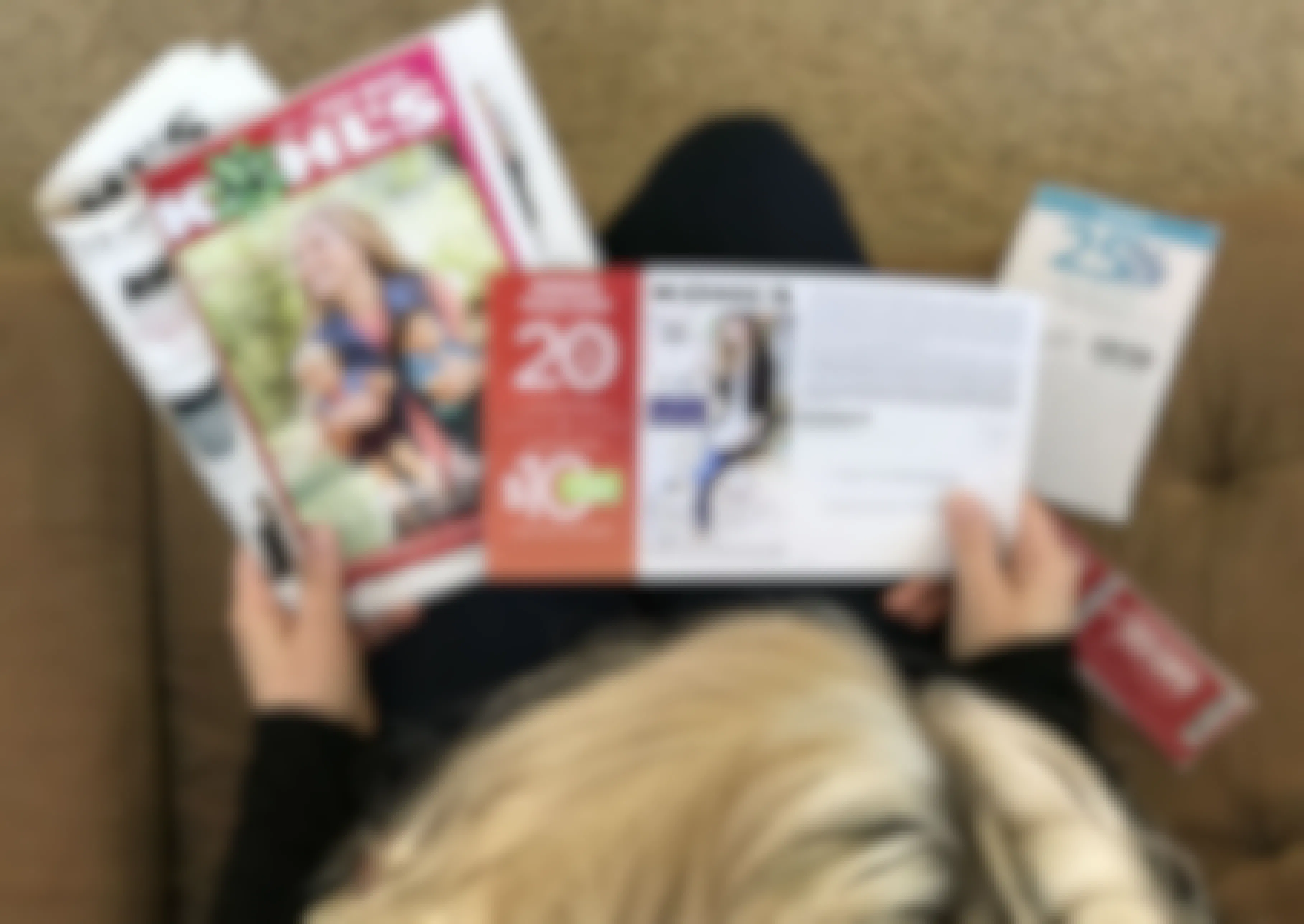 A person sitting on a couch, looking at some Kohl's coupons and an ad.