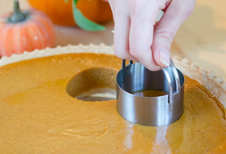 A person pushing a biscuit cutter into the middle of a pumpkin pie to make mini-pies.