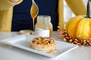 A person using a spoon to drizzle caramel sauce on a small pecan pie.