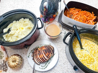 A mix of slow cookers filled with thanksgiving dinner sides on a counter.