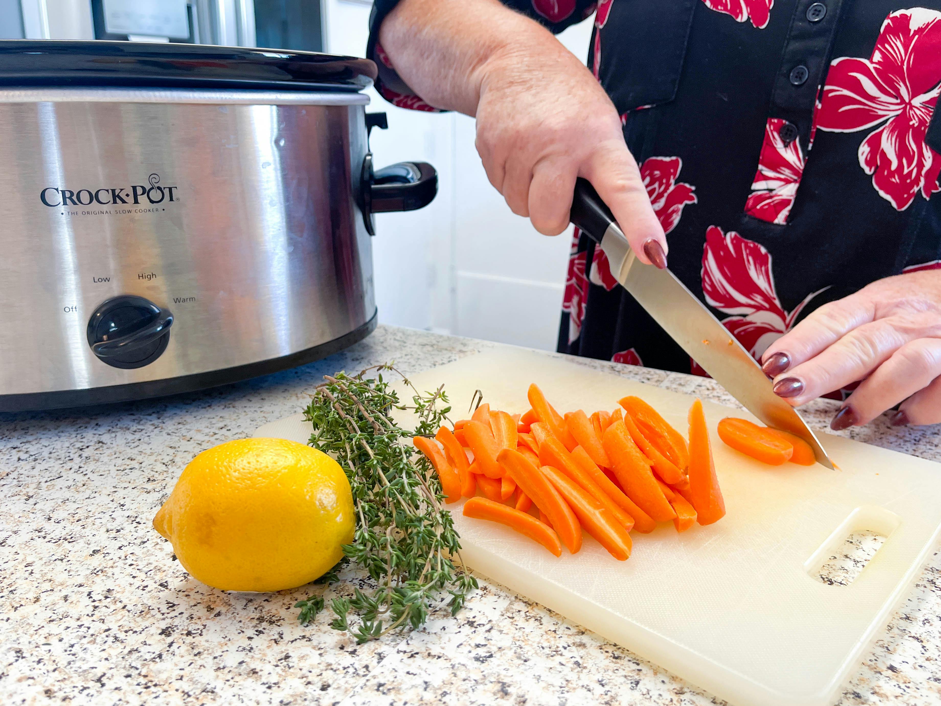a woman cutting up carrots for lemon thyme carrots in front of a crock pot.