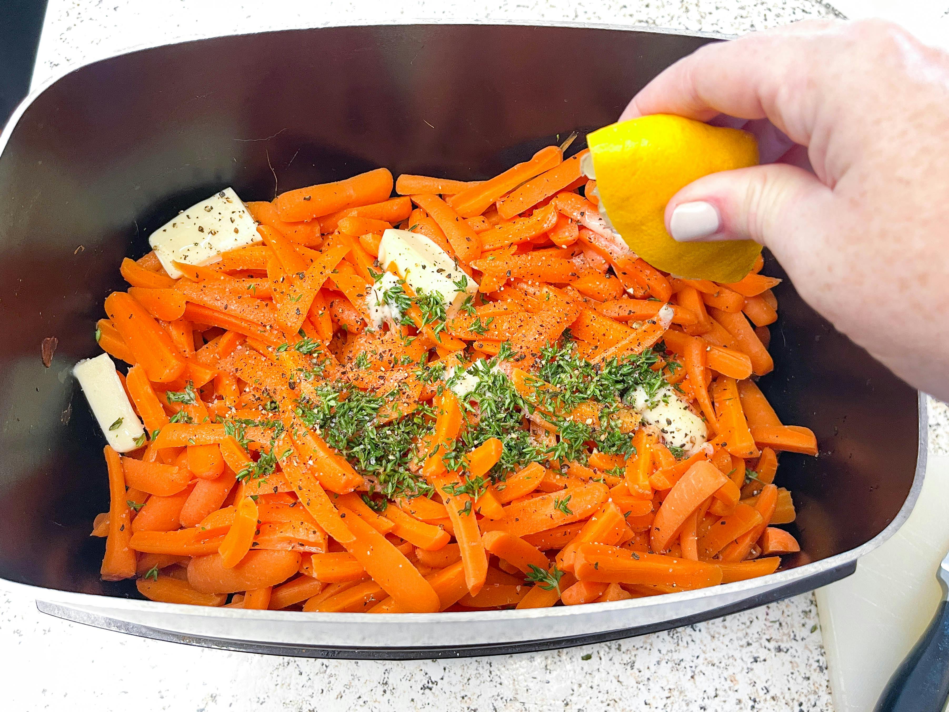 a person's hand squeezing lemon into a slow cooker filled with carrots, butter, and thyme.