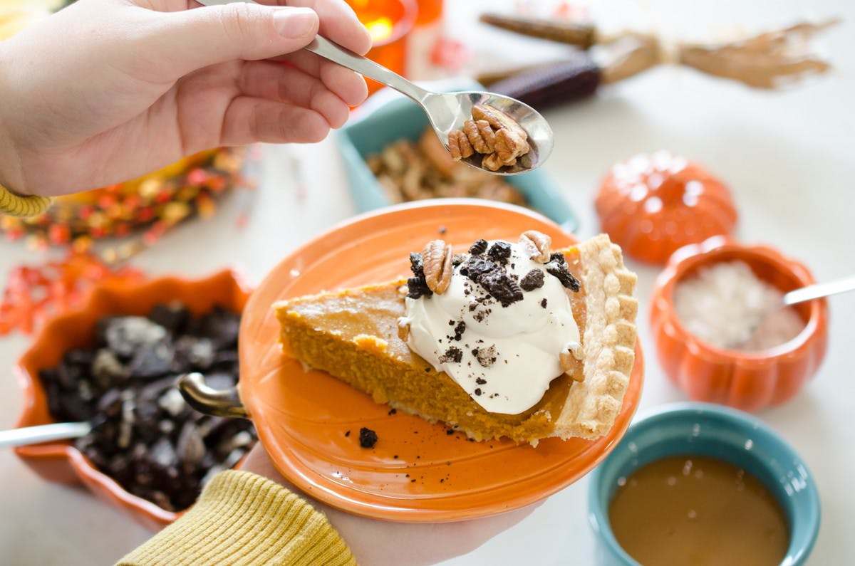 A person spooning toppings onto their plate of pumpkin pie and whipped cream.