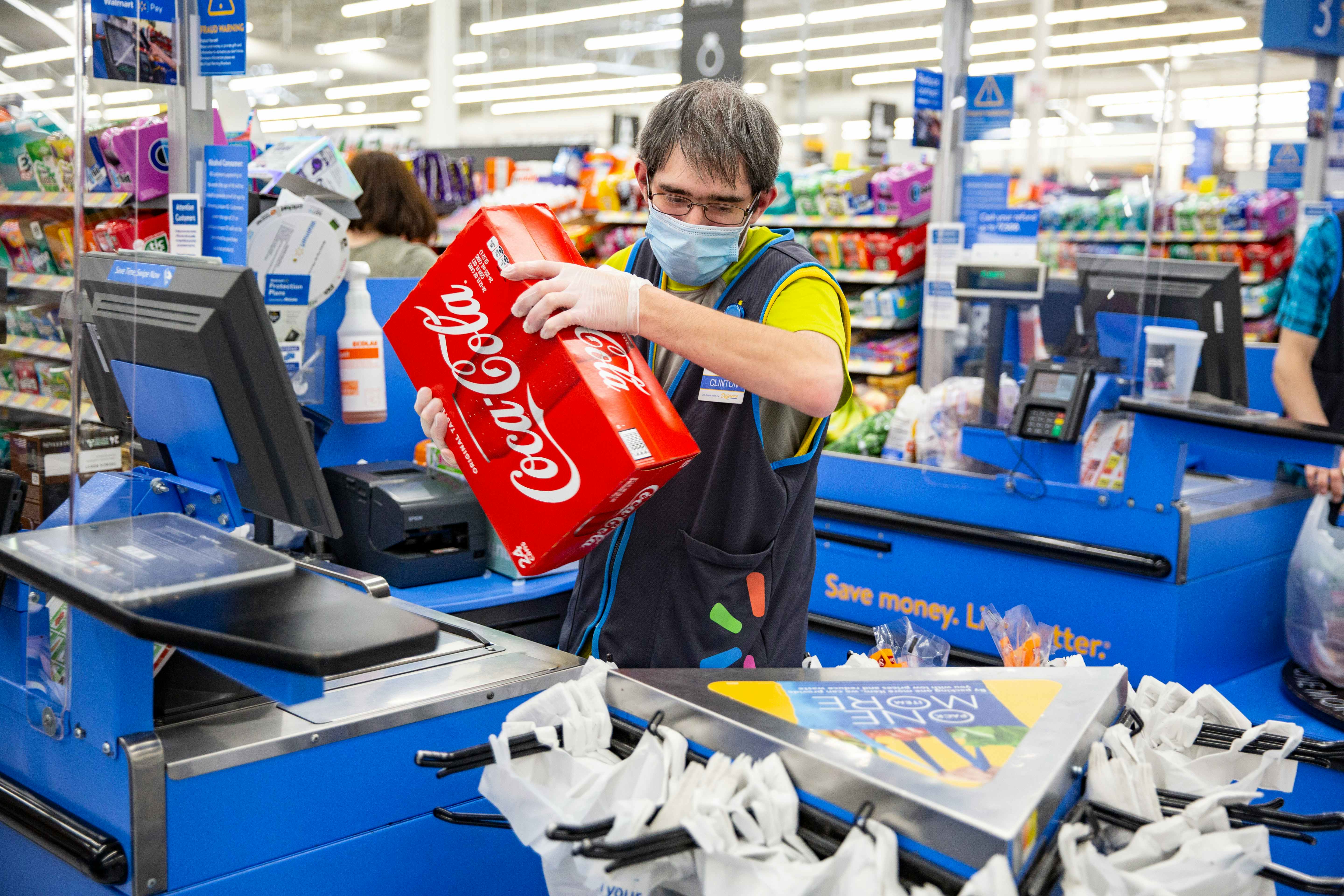 Walmart Employee wearing a mask and gloves ringing up a case of Coke at checkout.