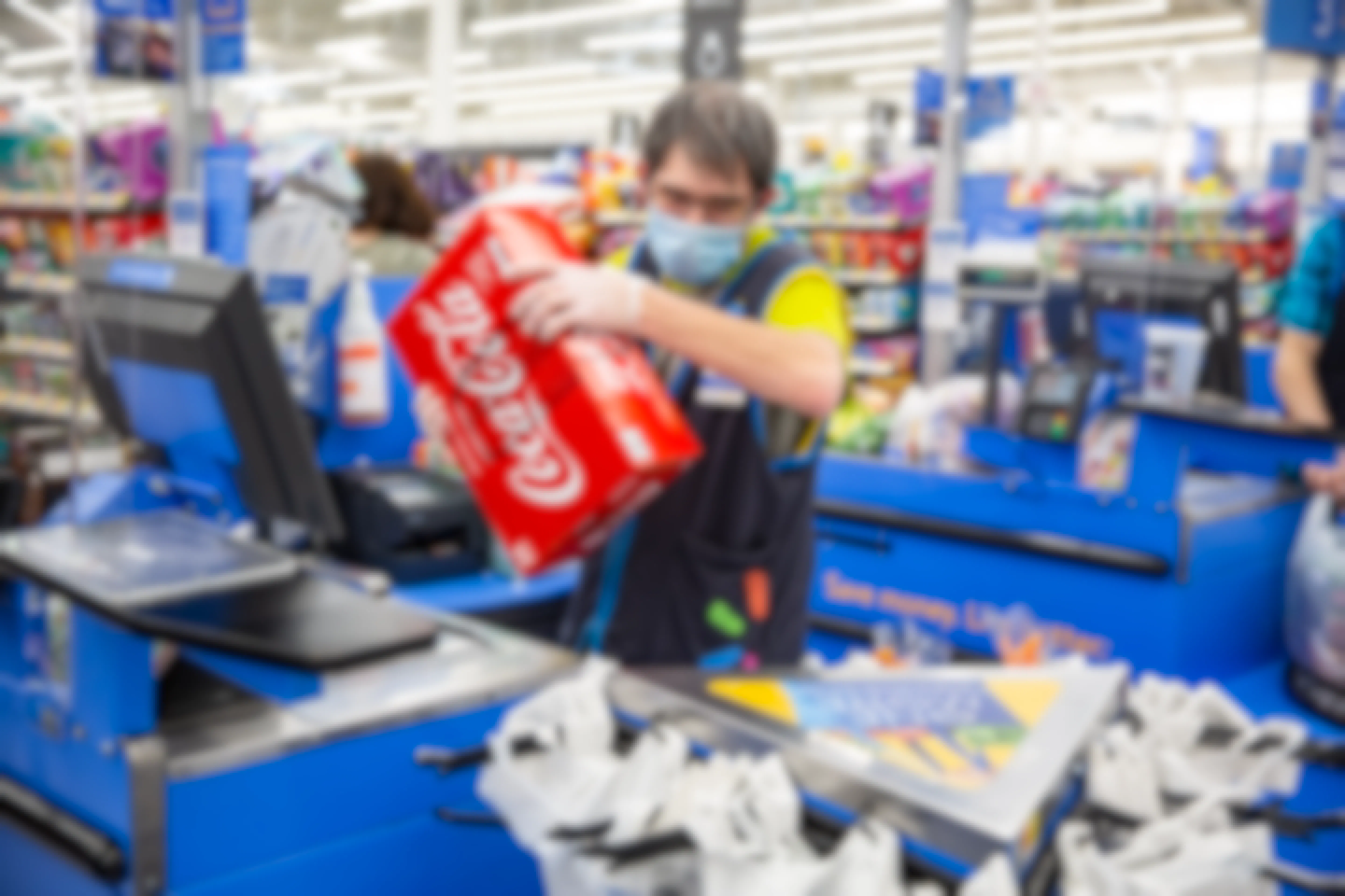 Walmart Employee wearing a mask and gloves ringing up a case of Coke at checkout.