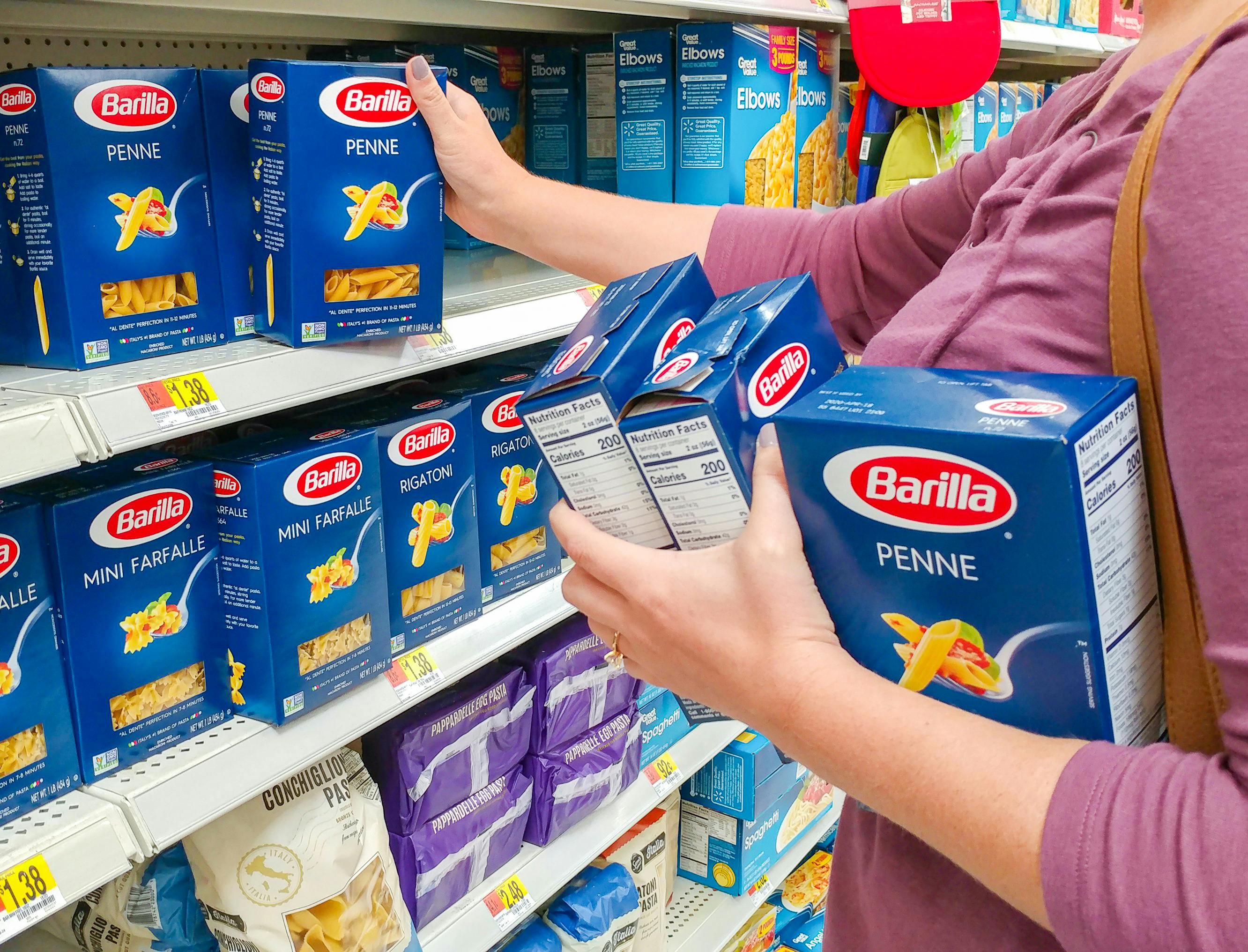 A woman taking boxes of Barilla pasta from a shelf in a grocery store.