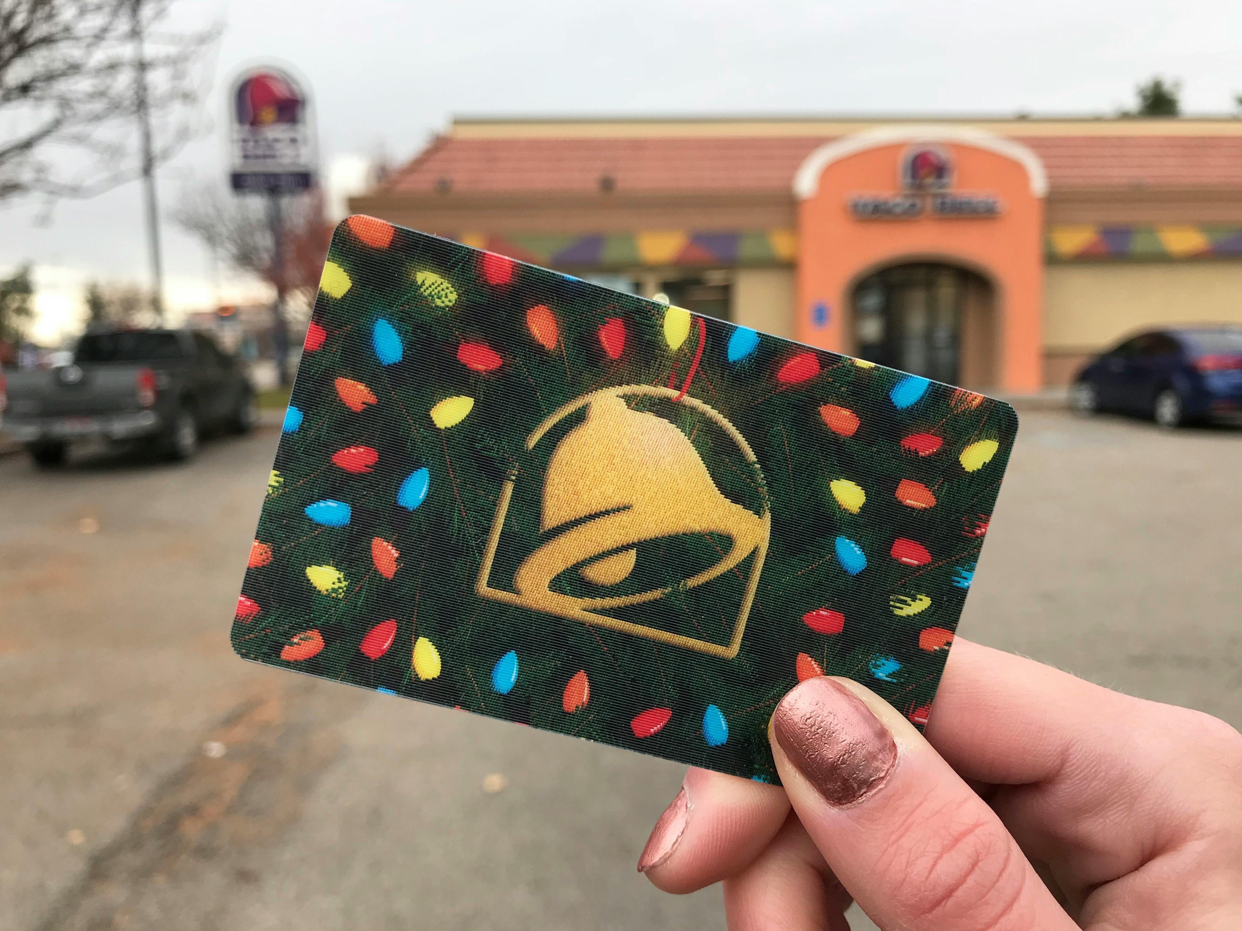 A Taco Bell gift card being held up in front of a Taco Bell restaurant.
