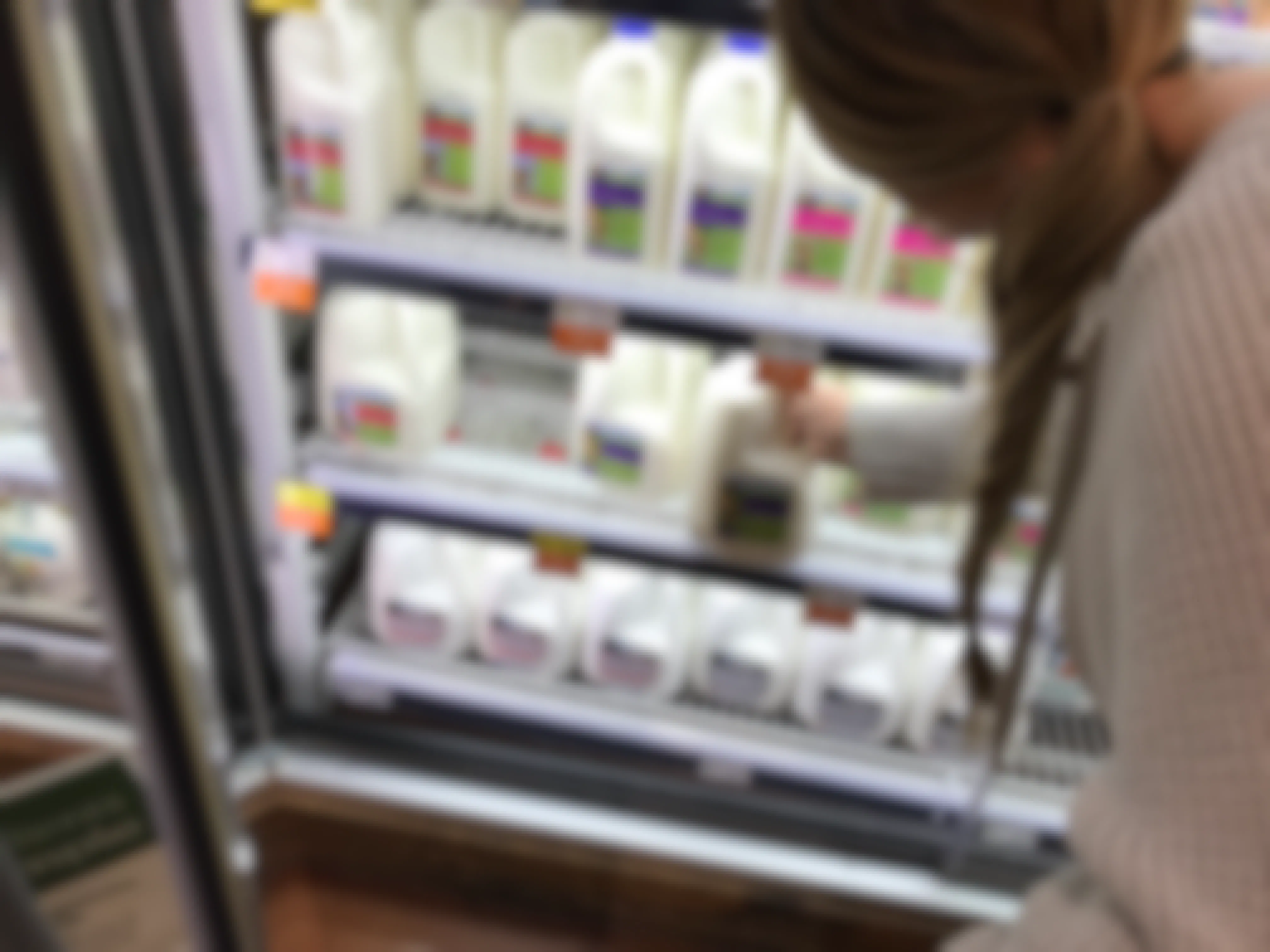 Woman reaching into a refrigerated case to grab a gallon of milk in a grocery store.
