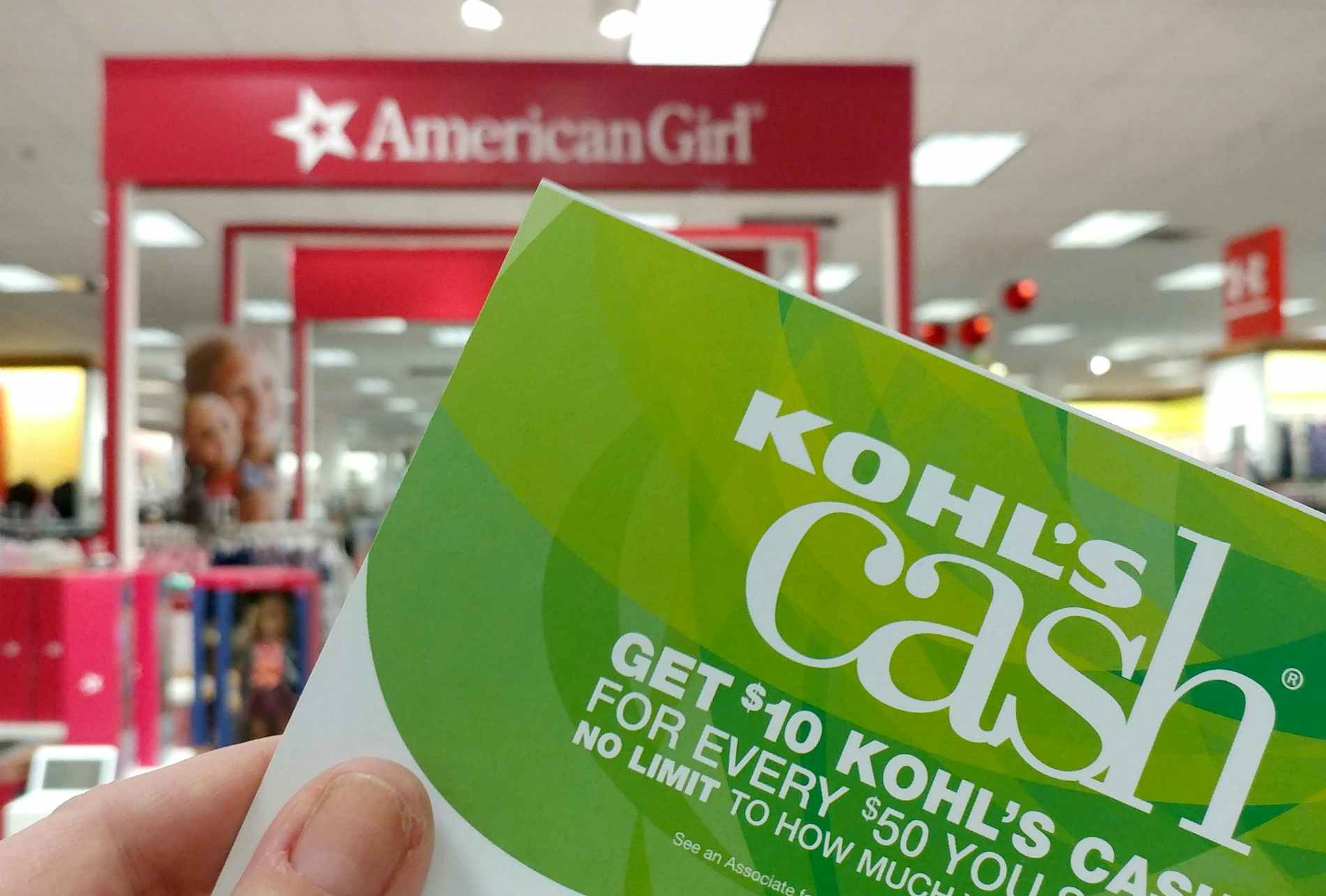 someone holding up Kohls Cash sign in front of American Girl Doll sign