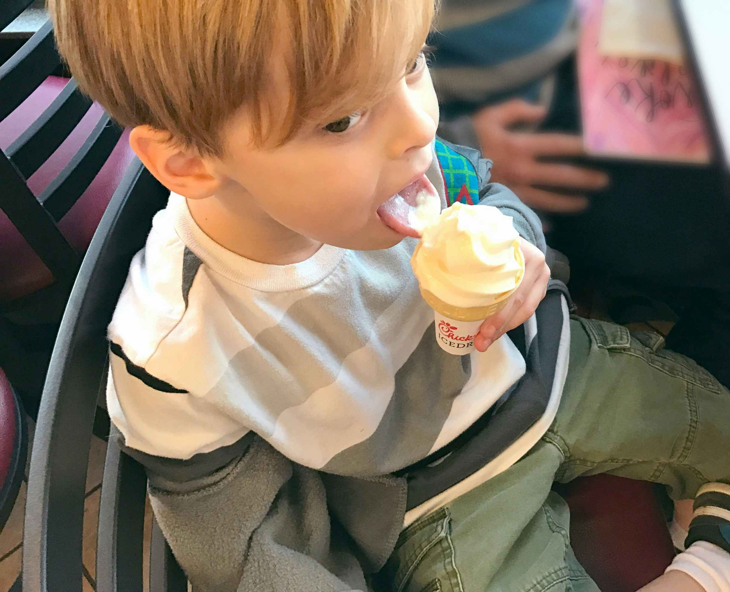 A child sitting inside Chick-fil-A, eating a soft serve ice cream on a cone.