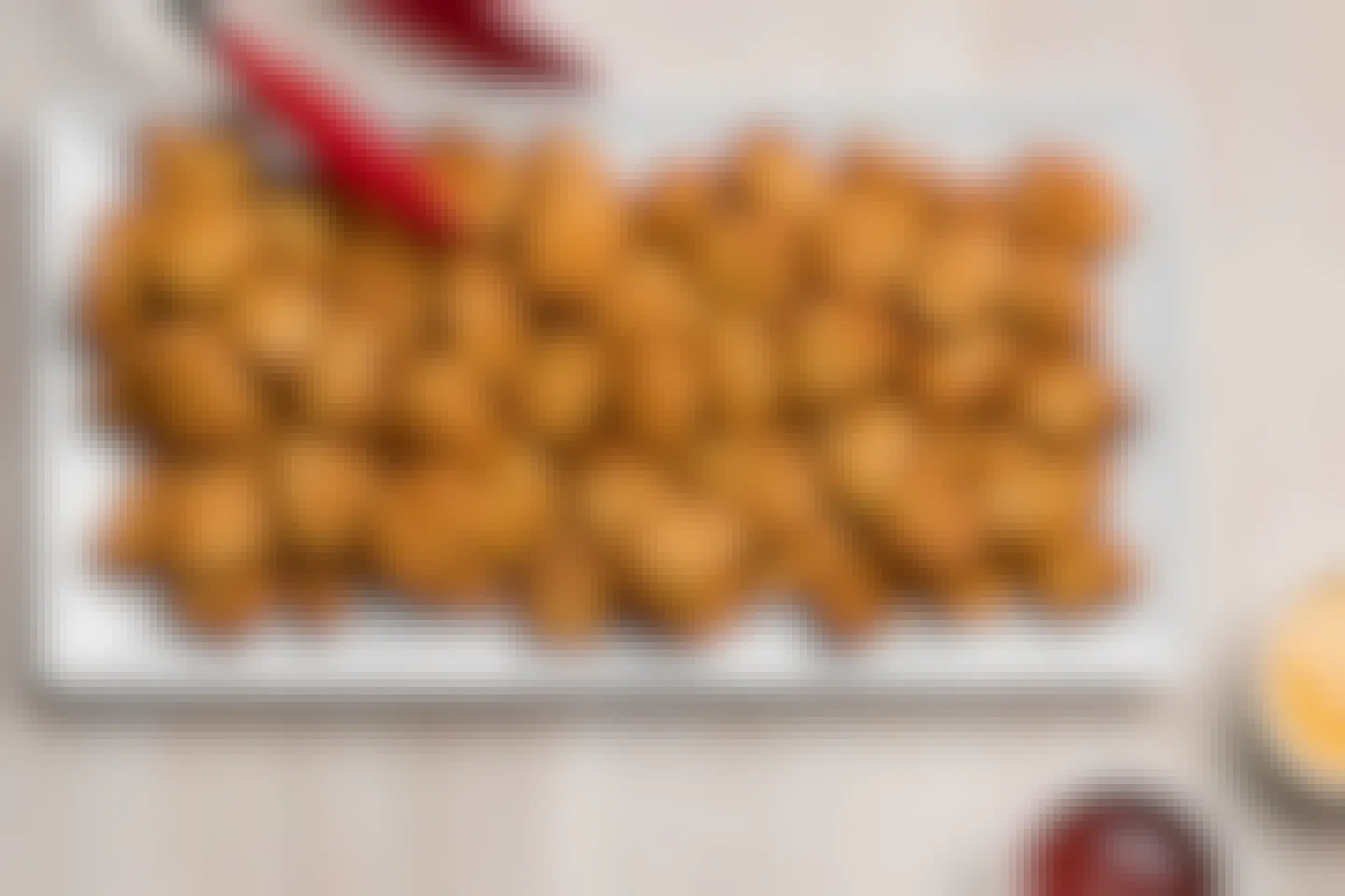 A large platter of Chick-fil-A chicken nuggets on a table next to some tongs and dipping sauces.