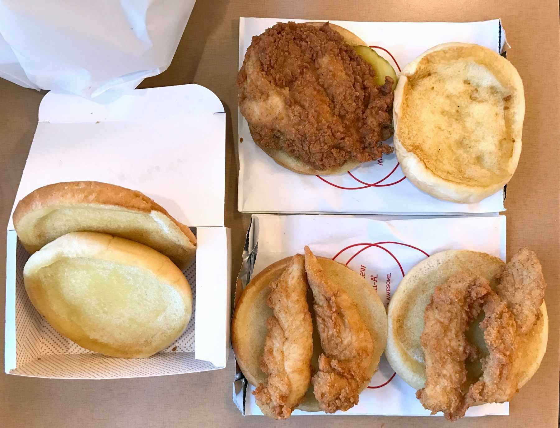 A Chick-fil-A chicken sandwich on a table next to some buns with Chick-fil-A chicken tenders on them.