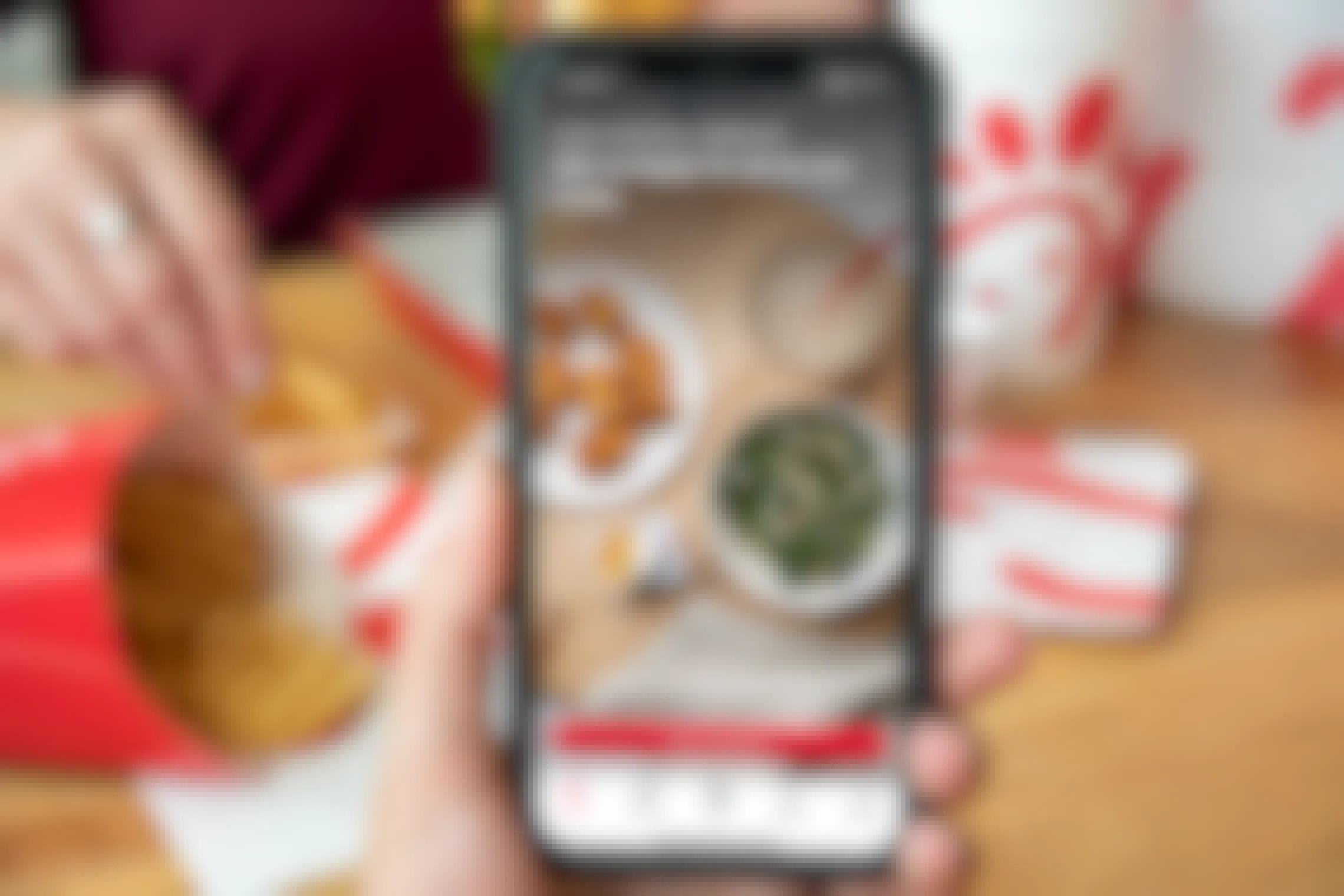 Chick-fil-a app on a cell phone with a person eating chick-fil-a in the background.