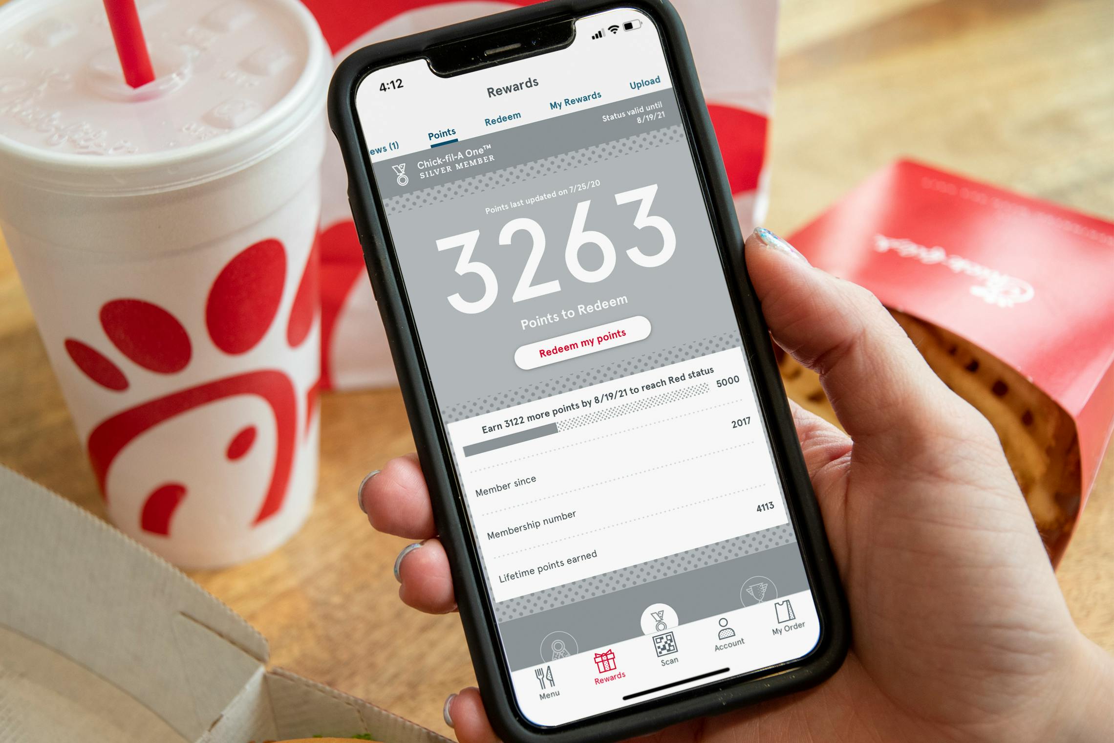 A person's hand holding a cell phone displaying their points on the Chick-fil-A app in front of a Chick-fil-A meal on the table.