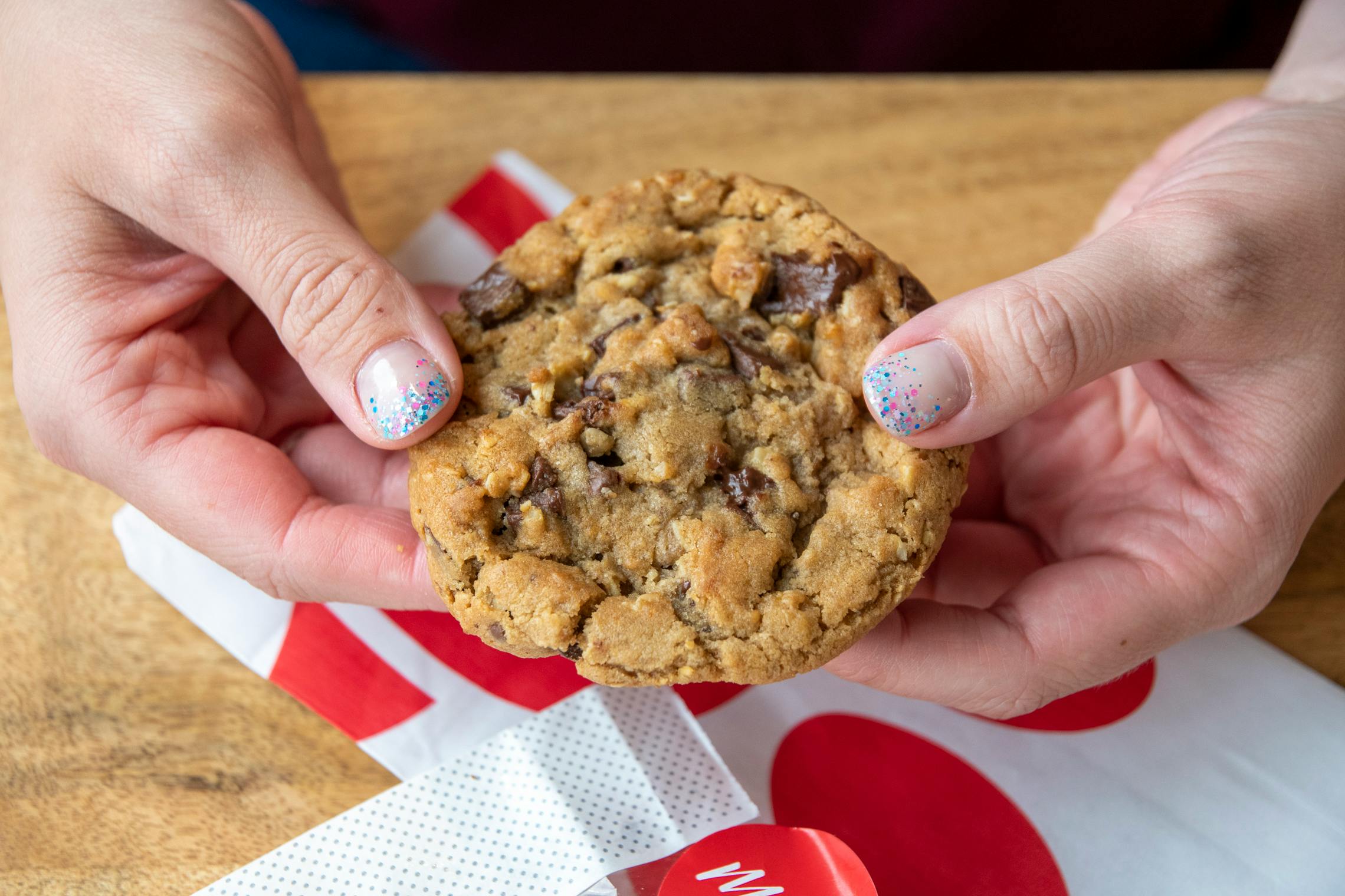 A person's hands holding a Chick-fil-A chocolate chunk cookie over a table.