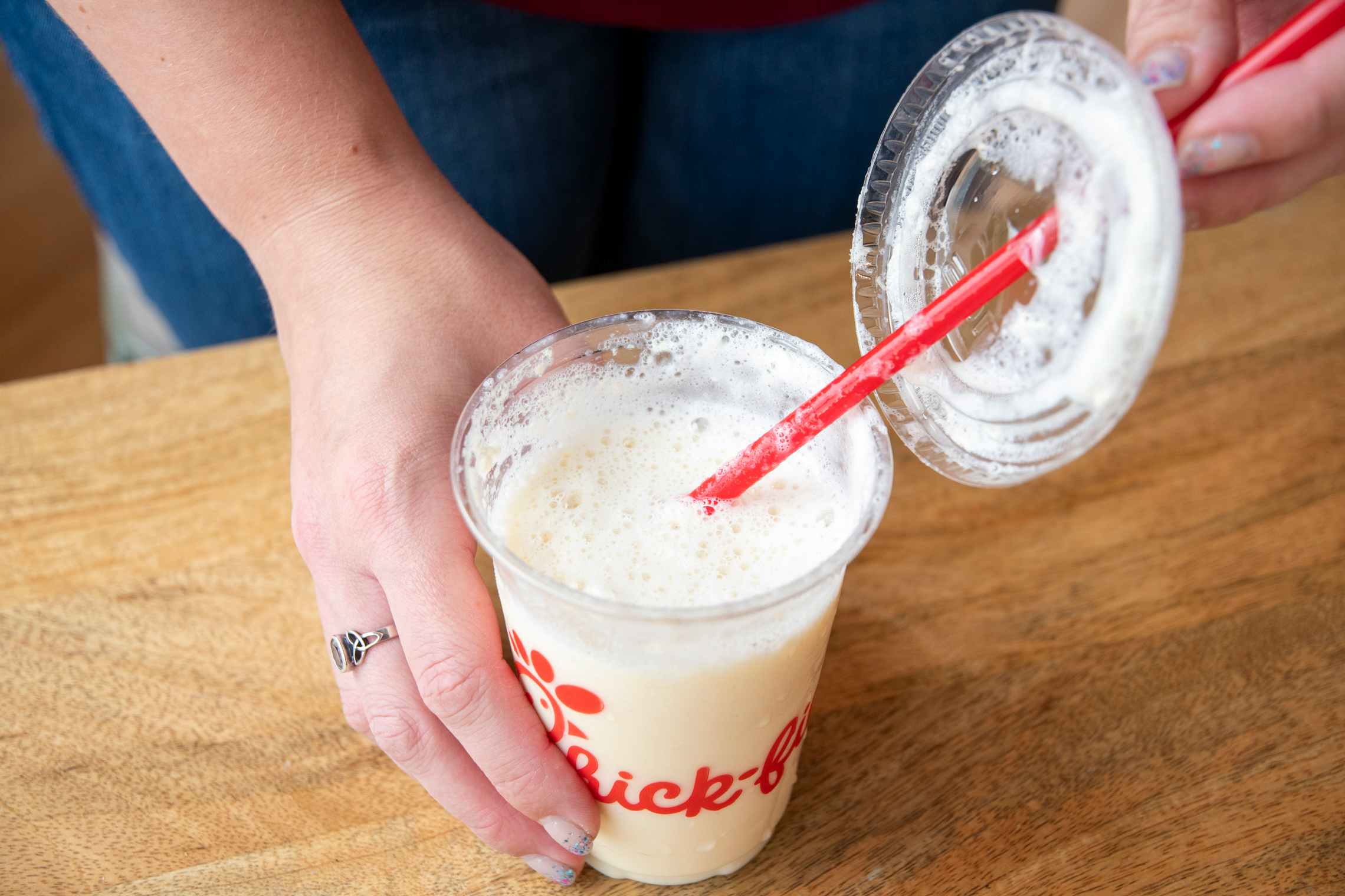 A frosted Chick-fil-A drink with a person taking the lid off off the cup.