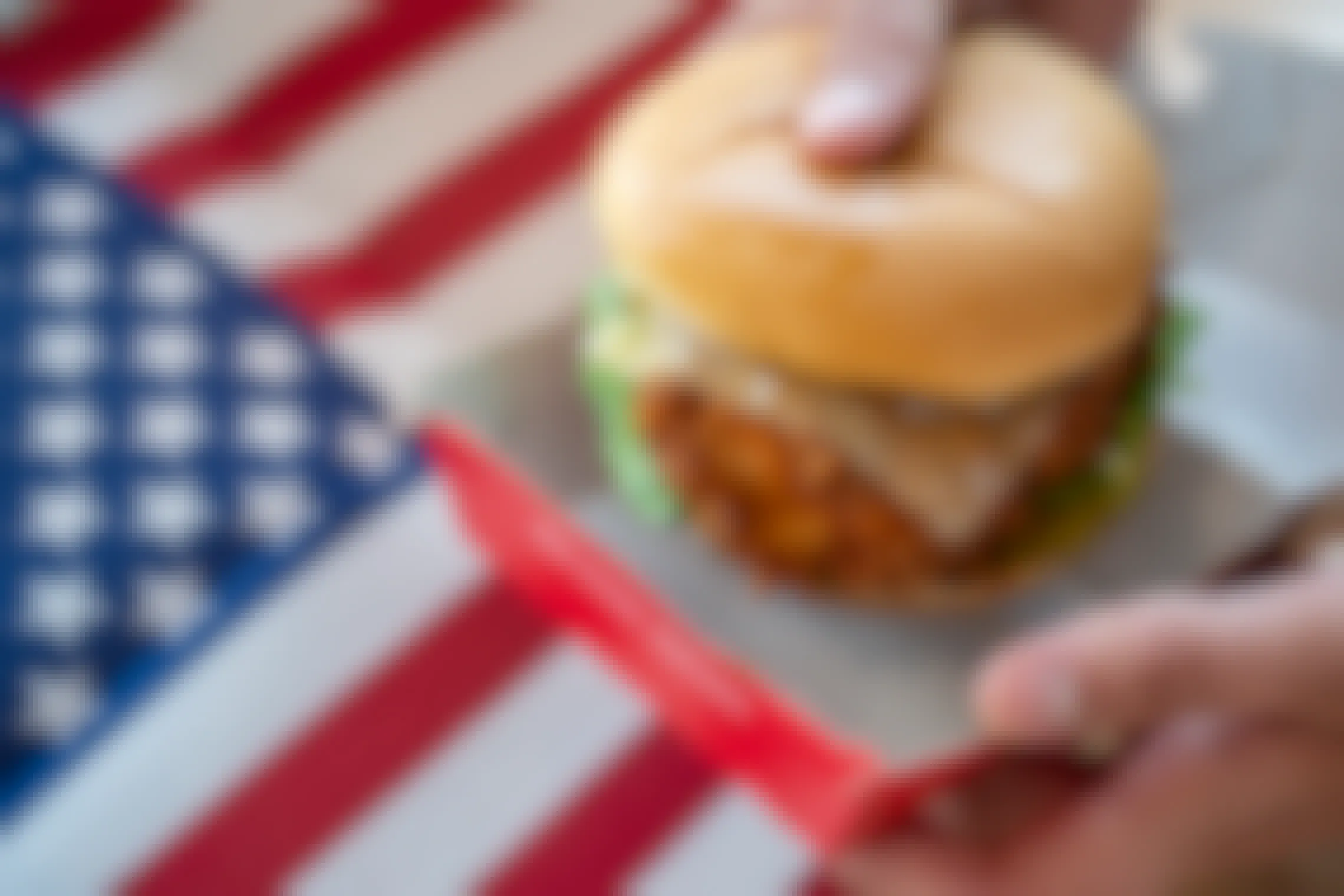 A Chick-fil-A chicken sandwich being held above an American flag.