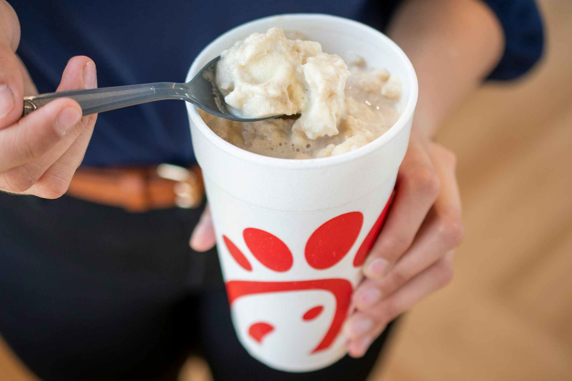 A person using a spoon to scoop ice cream from a root beer float in a Chick-fil-a cup.